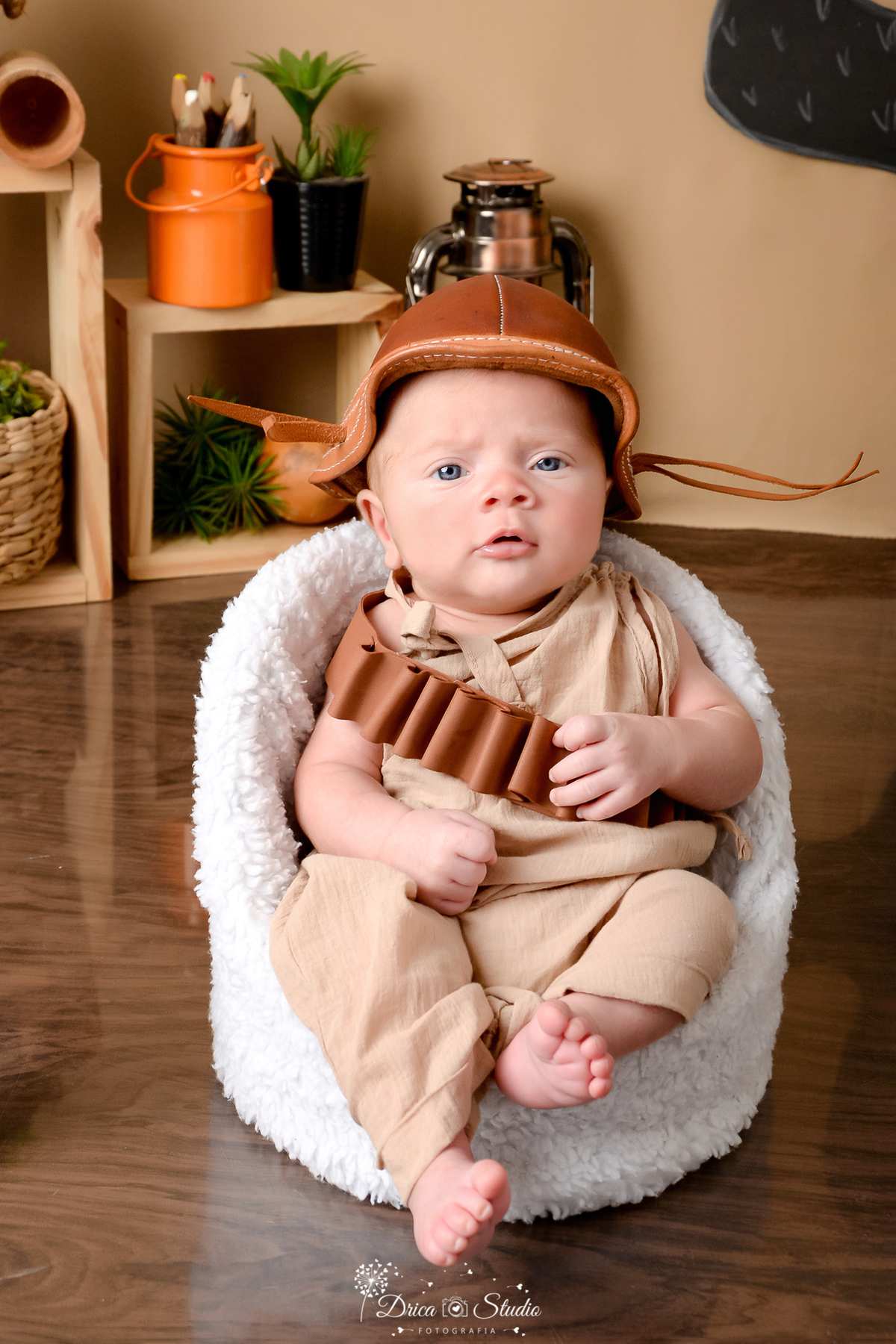 drica studio - ensaio fotografico infantil - tema sertão nordestino - bebê sentado em poltrona branca, vestindo macaquinho bege - chapéu de cangaceiro - nicho de madeira - fundo de cordel - cabaça - cesto de palha com arbustos