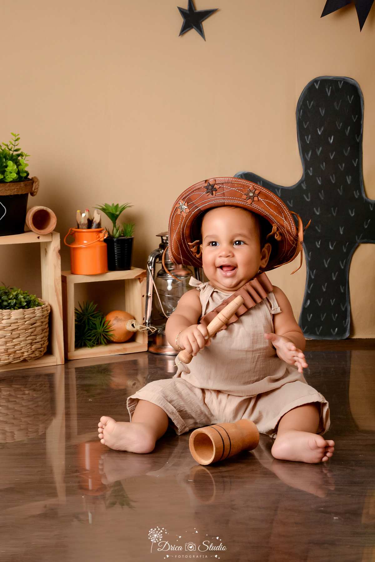drica studio - ensaio fotografico infantil - tema sertão nordestino - bebê sendado no chão segurando mão de pilão de madeira - latão de leite laranjado - nicho de madeira - cesto de palha com arbustos dentro - fundo de cordel -  chapéu de cordel