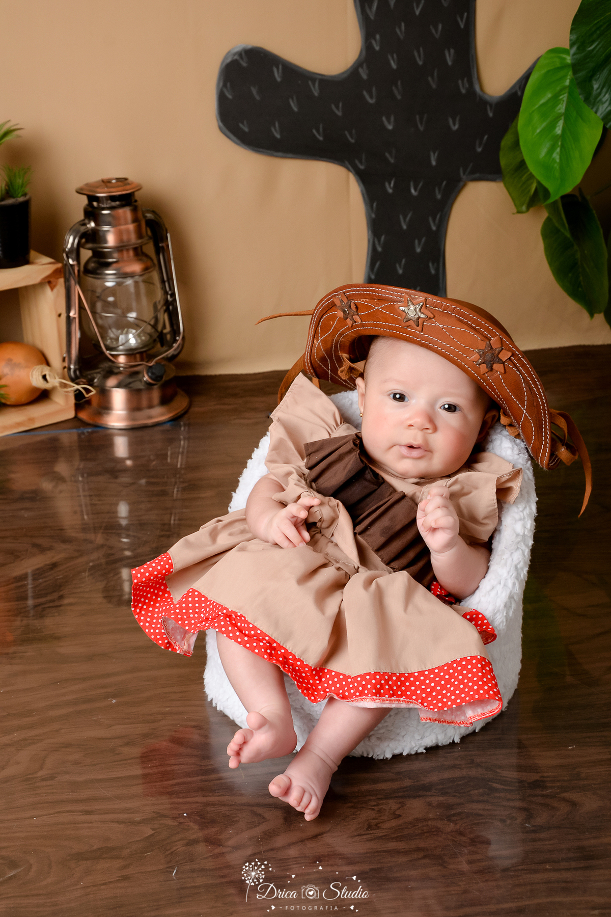 drica studio - ensaio fotografico infantil - tema sertão nordestino - bebê vestida de maria bonita usando chapéu de cordel - lampião antigo - nicho de madeira - piso amadeirado - cabaça - poltrona branca