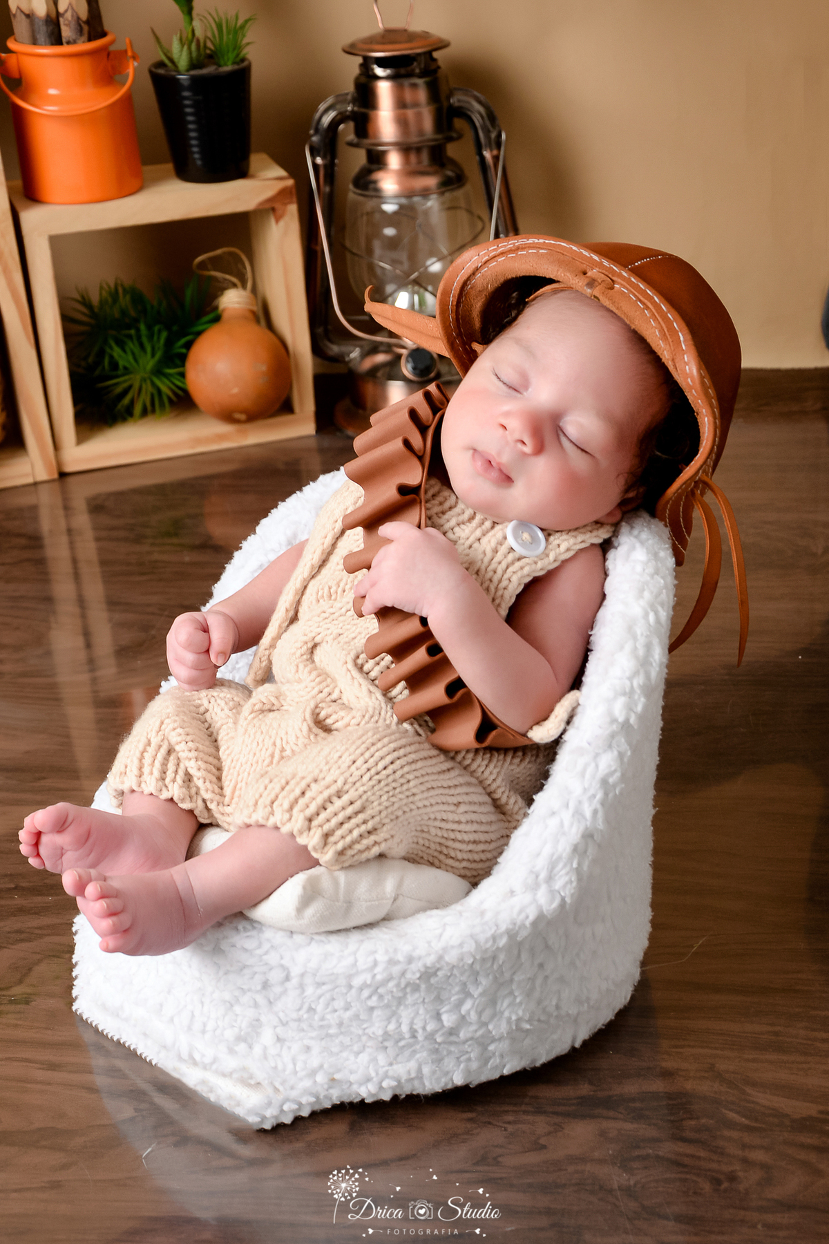 drica studio - ensaio fotografico infantil - tema sertão nordestino - bebê usando cinto de bala e chapéu de cangaceiro - macaquinho de tricô bege - poltrona branca - piso amadeirado - nicho de madeira - lampião antigo