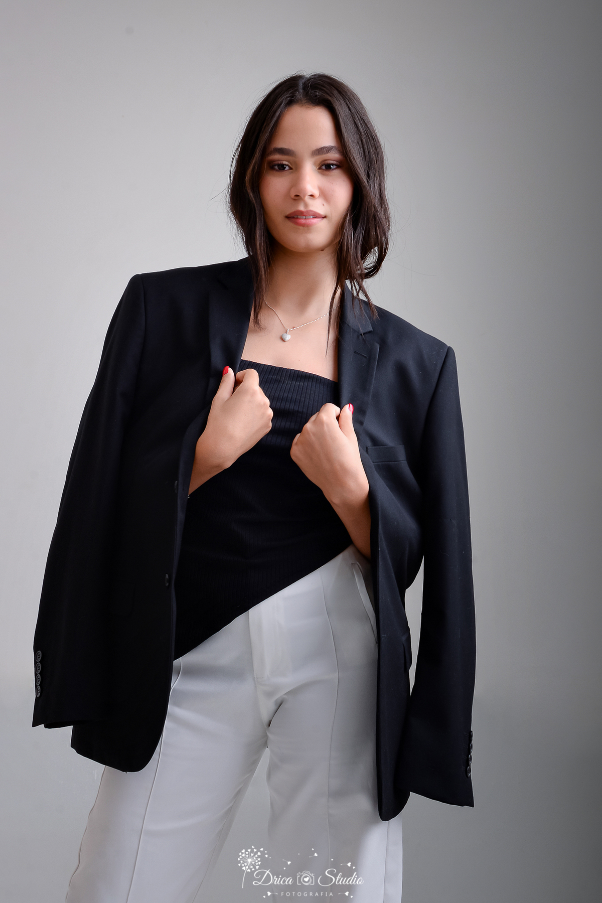 drica studio - ensaio fotográfico - aniversárlo 19 anos - xinguara -mulher vestindo uma calça branca , blusa preta justa e um blazer preto que está levemente caído nos ombros, cabelo é castanho escuro, solto e levemente ondulado