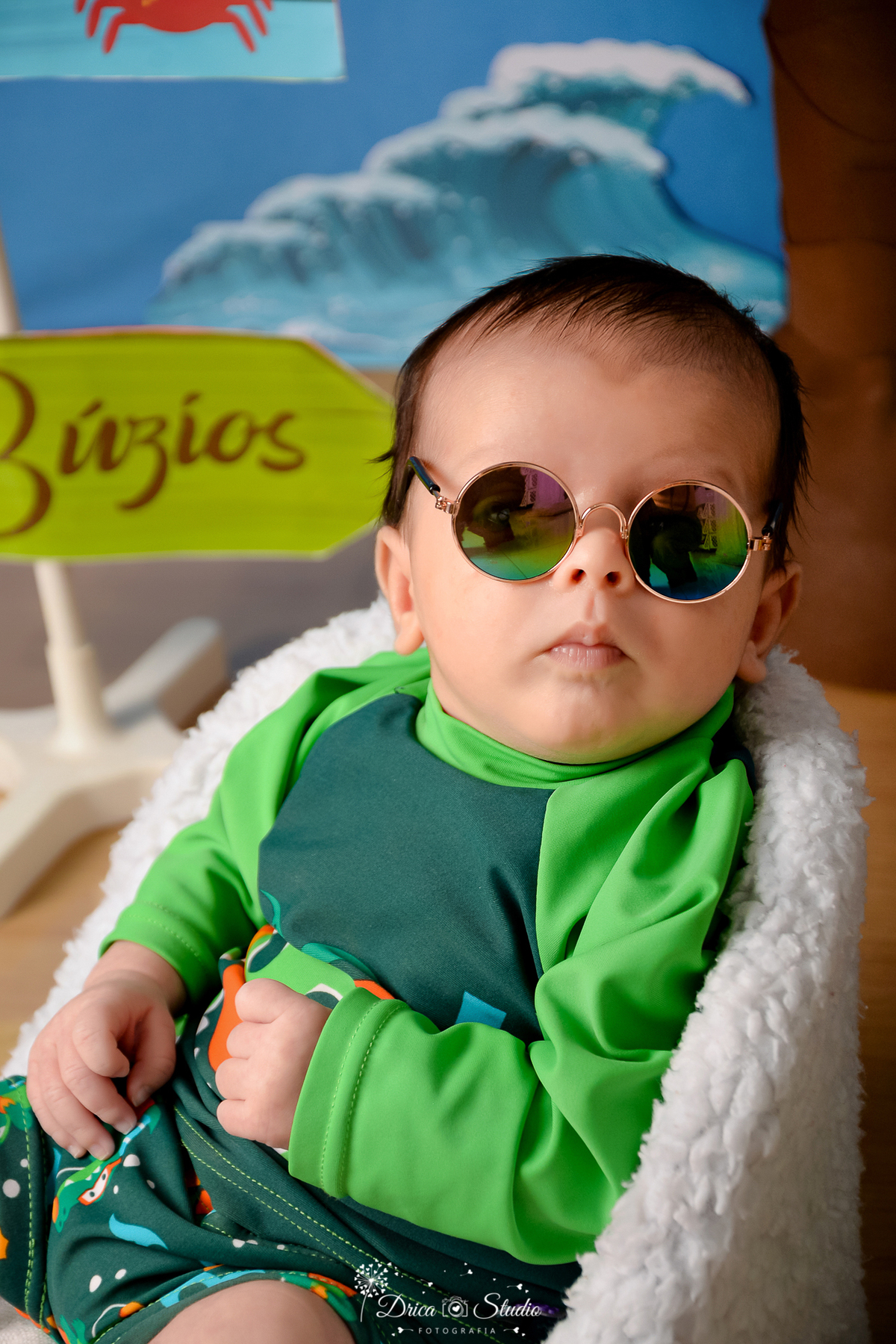 drica studio - ensaio fotográfico infantil - verão e praia - bebê vestindo camisa termica de praia, usando óculos de sol, sentado em poltrona branca felpuda - plaquinha com nome búzios 