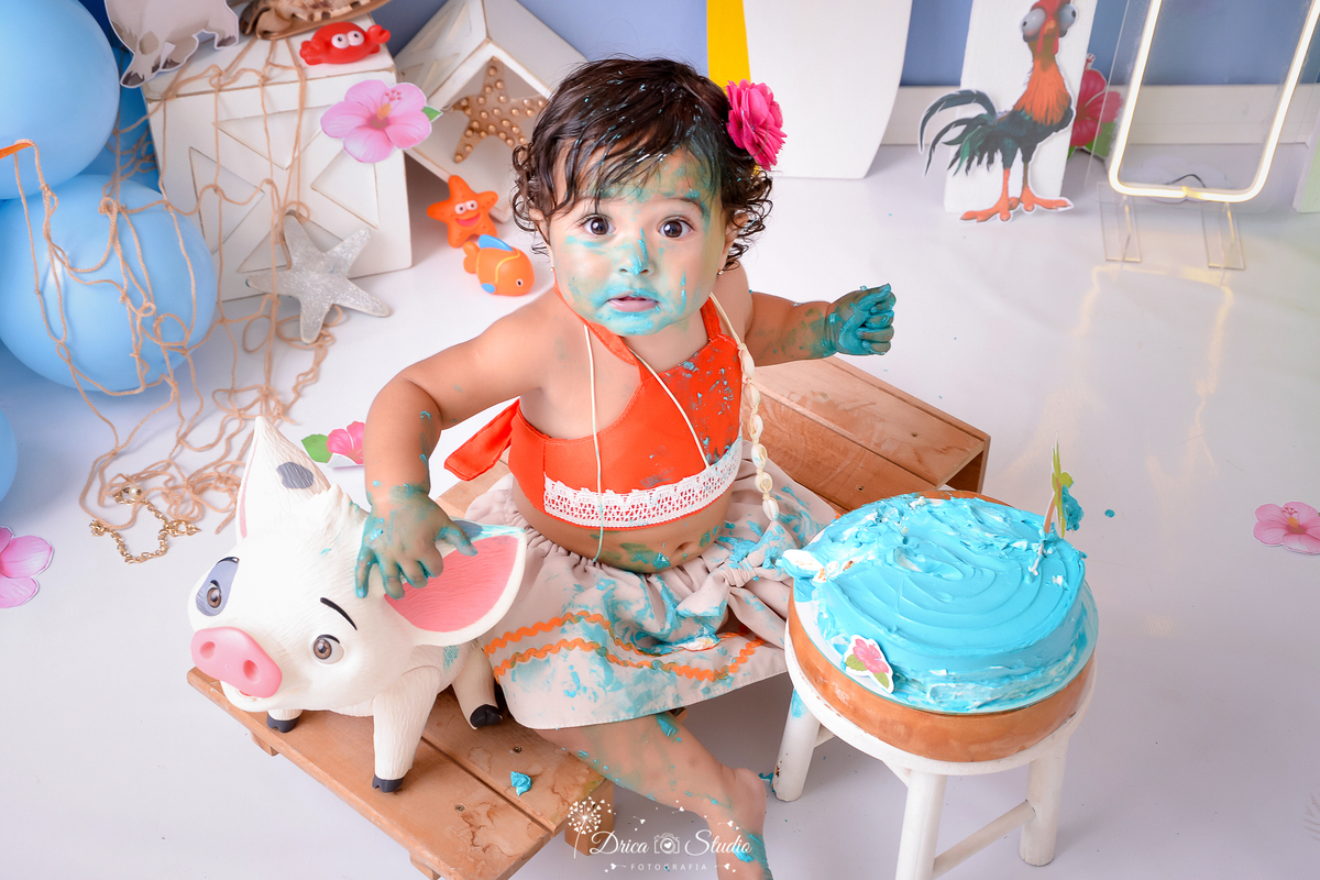 drica studio - ensaio fotografico infantil - smash the cake moana baby - xinguara - bebê sentada em barquinho com a segurando um porquinho de brinquedo - bolo azul sobre um baquinho branco - caixote branco- rede de corda - esterla do mar - fundo azul