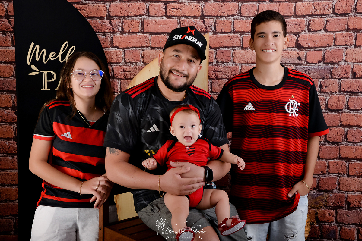 drica studio - ensaio fotografico dia dos pais - xinguara - pai e filhos usando camisa do flamengo, pais seguando bebê no colo, filha em pé ao seu lado direito e filho do lado esquerdo - fundo de tijolos vermelho e painel preto.