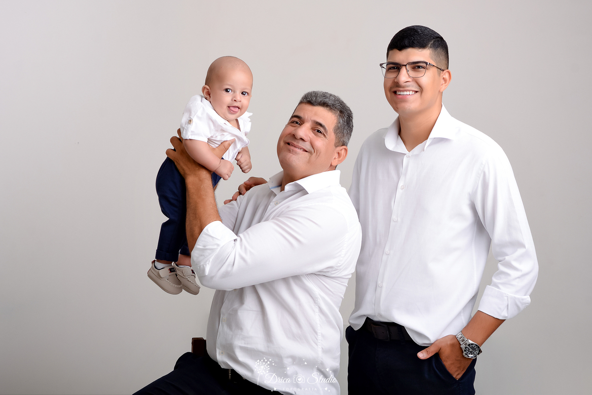 drica studio - ensaio fotografico dia dos pais - xinguara - avô segurando neto no ar, sentado ao lado do filho - camisa branca - calça jean azul - fundo cinza - relogio de pulso - óculos de grau