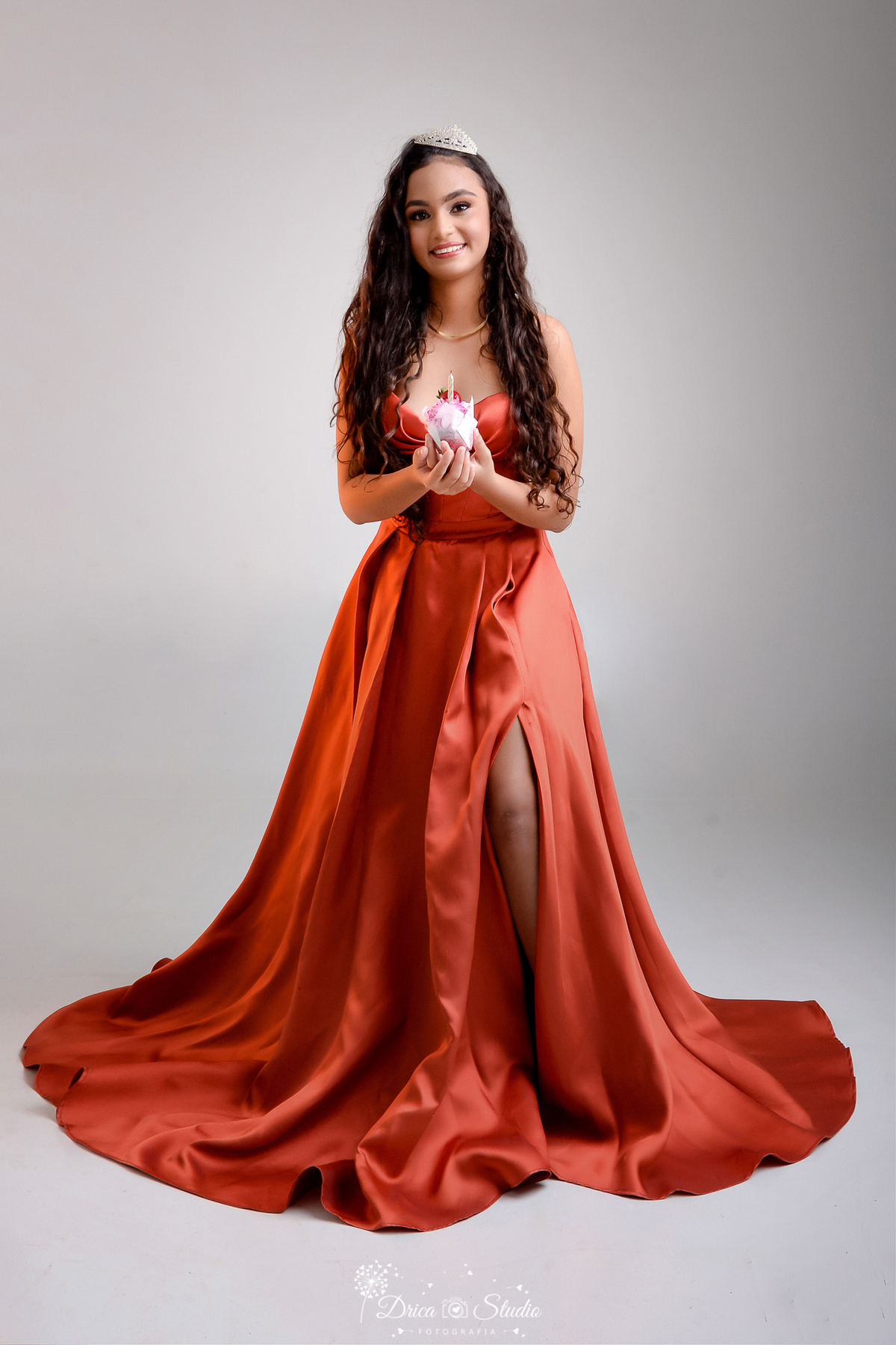 drica studio - ensaio fotográfico 15 anos - xinguara -jovem usando vertido em tom terroso, de tecido acentinado, corpete estruturado e saia longa, usando brindo e colar descreto  - tiara de brilhantes - capcake - fundo neutro