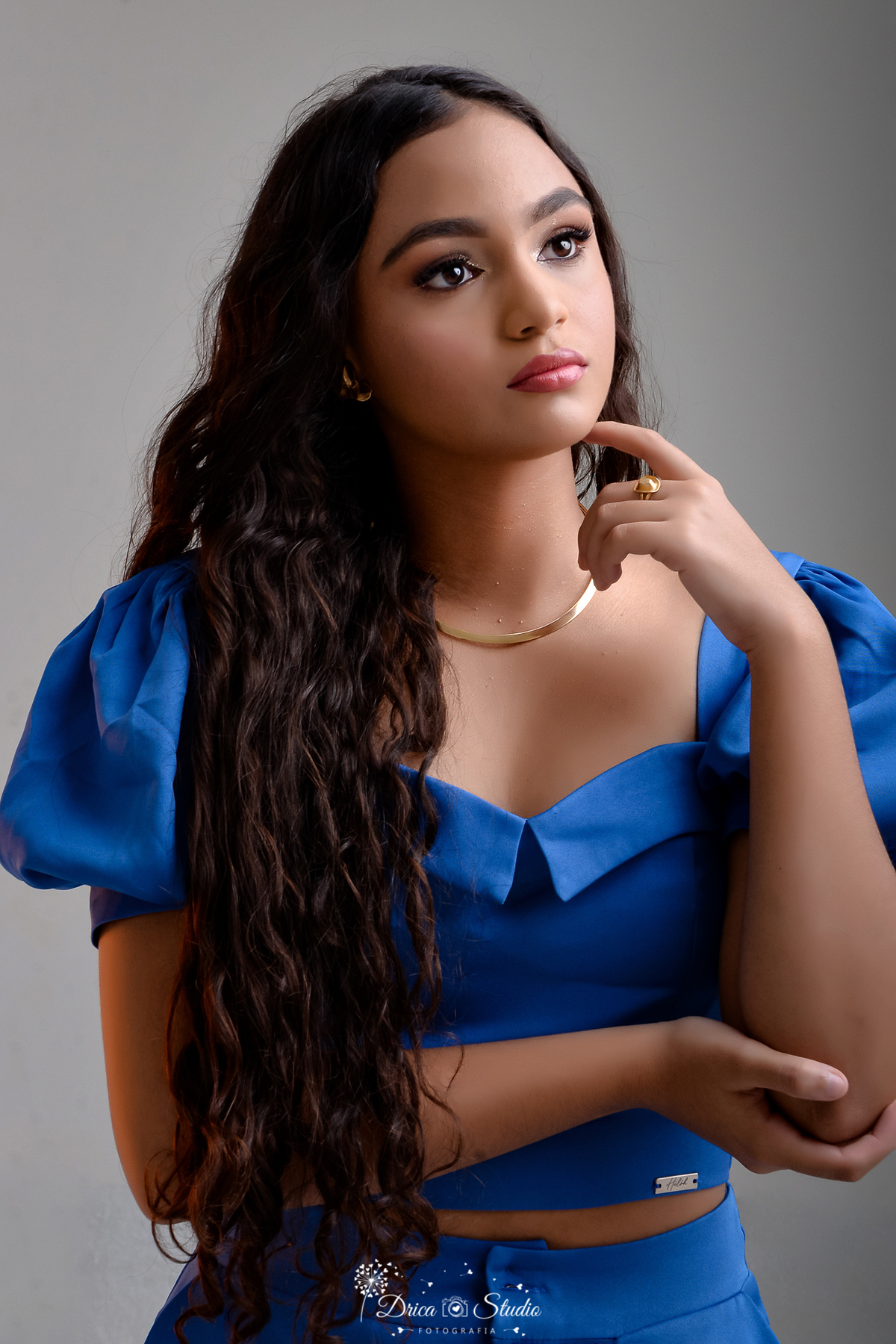 drica studio - ensaio fotográfico 15 anos - xinguara - jovem de cabelos longo e cacheados usando blusa azul com mangas bulfantes e colar dourado - fundo cinza claro