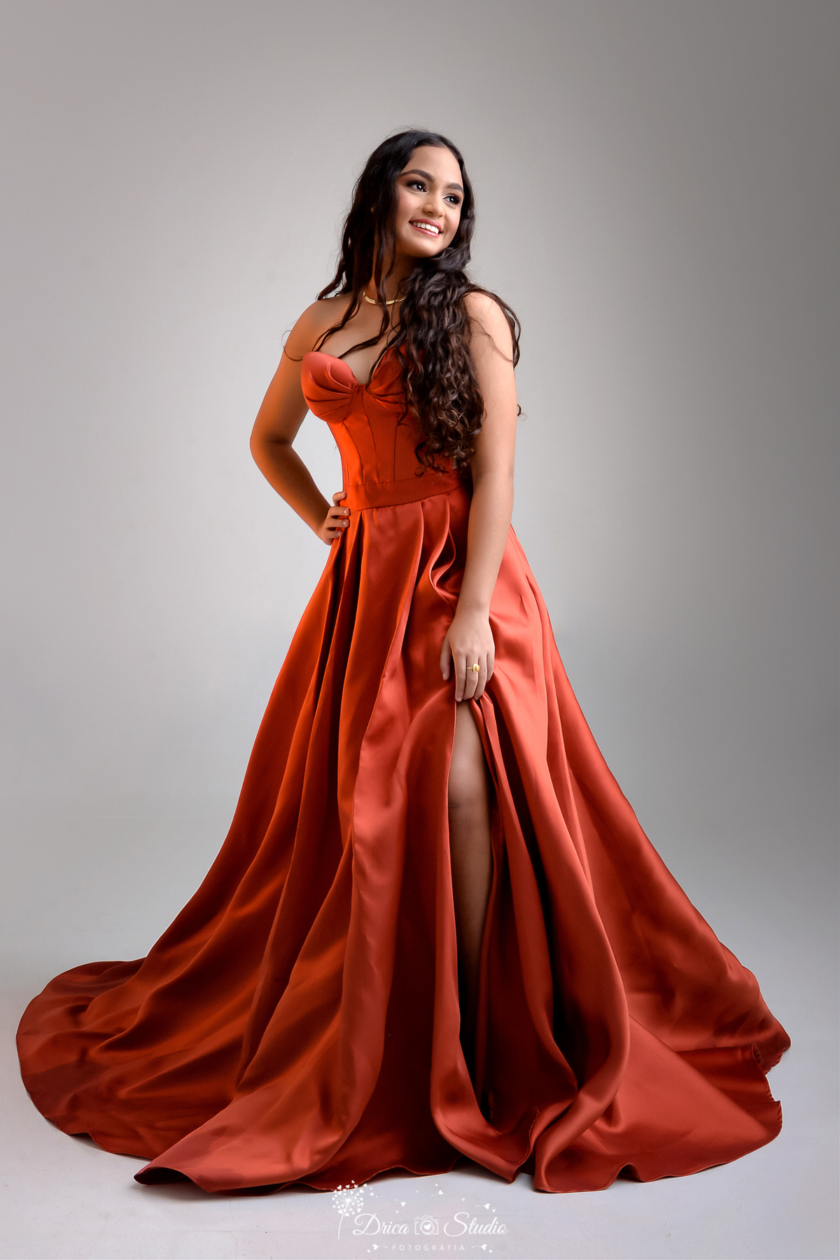 drica studio - ensaio fotográfico 15 anos - xinguara - jovem de cabelo longos e cacheados caidos sobre o ombro, usando vestido tom terroso, de tecido acetinado, com corpete estruturado e saia ampla - funco neutro