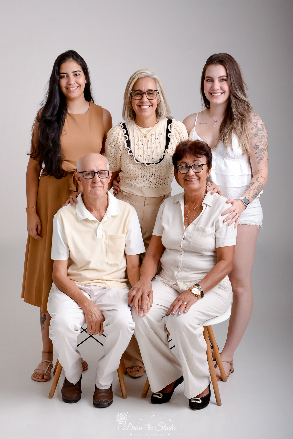 drica studio - ensaio fotografico - família - xinguara - casal sentado e atras deles três mulheres em pé - duas loiras e uma morena - blusa bege - blusa e short branco - vestido marrom - óculos de grau - fundo neutro