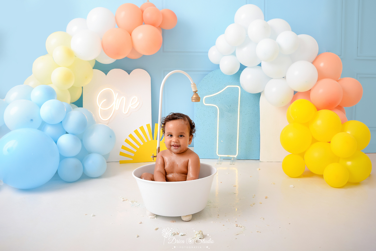 drica studio - ensaio fotografico infantil - smahs the cake - minha primeira volta ao sol - xinguara - bebê sentado dentro de banheira branca com chuveirinho - balão amarelo, coral, branco e azul - hum de led - one de led - painel branco - fundo azul - 
