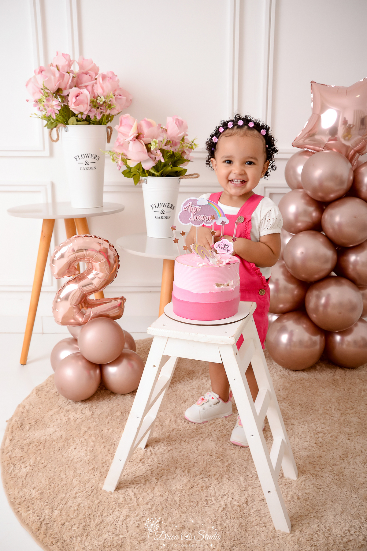 drica studio - ensaio fotografico infantil - aniversário de 2 anos - xinguara - bolo sobre banquinho branco - balão rose - jarro branco com flores rosa - menina vestindo macaquinho rosa pink e blusa branca - mesinha de canto - tapete felpudo - fundo neutr