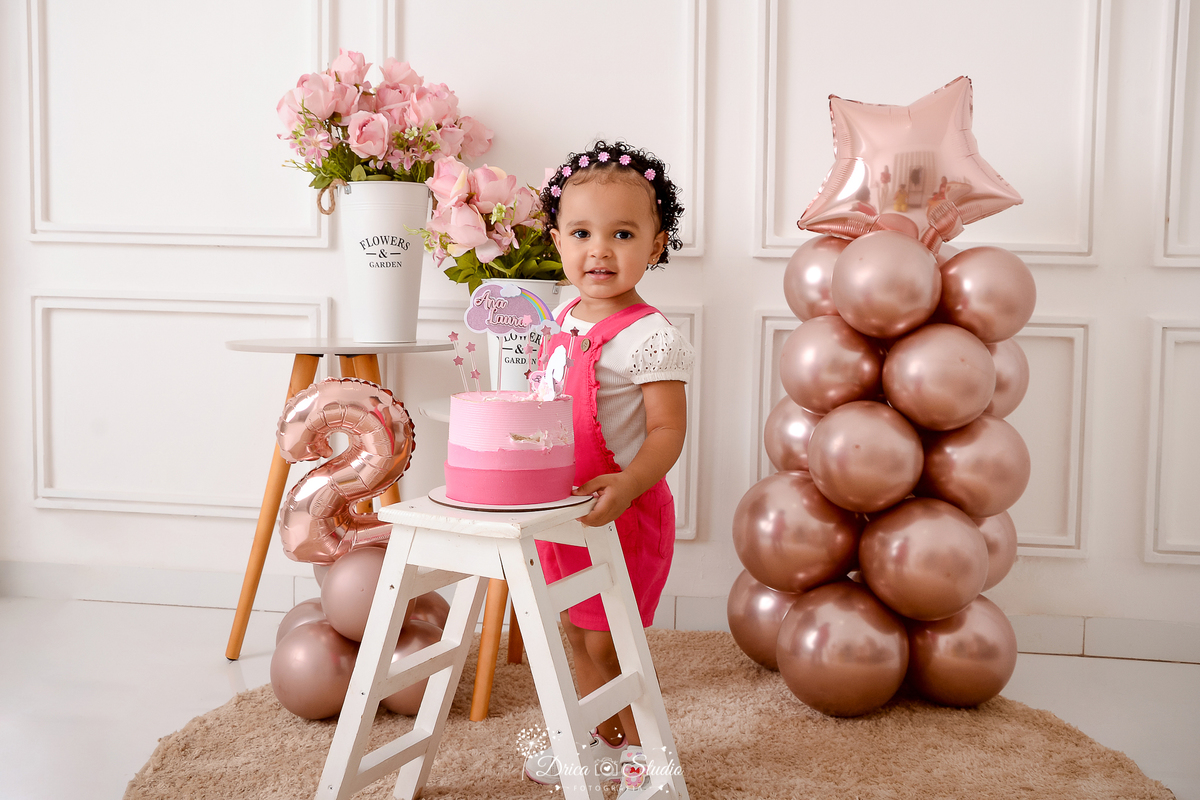 drica studio - ensaio fotografico infantil - aniversário de 2 anos - xinguara - menina vestindo macaquinho rosa pink e blusa branca - balão rose - banquinho branco e bolo em três tons de rosa - jarro com flores rosa - fundo neutro com boiserie