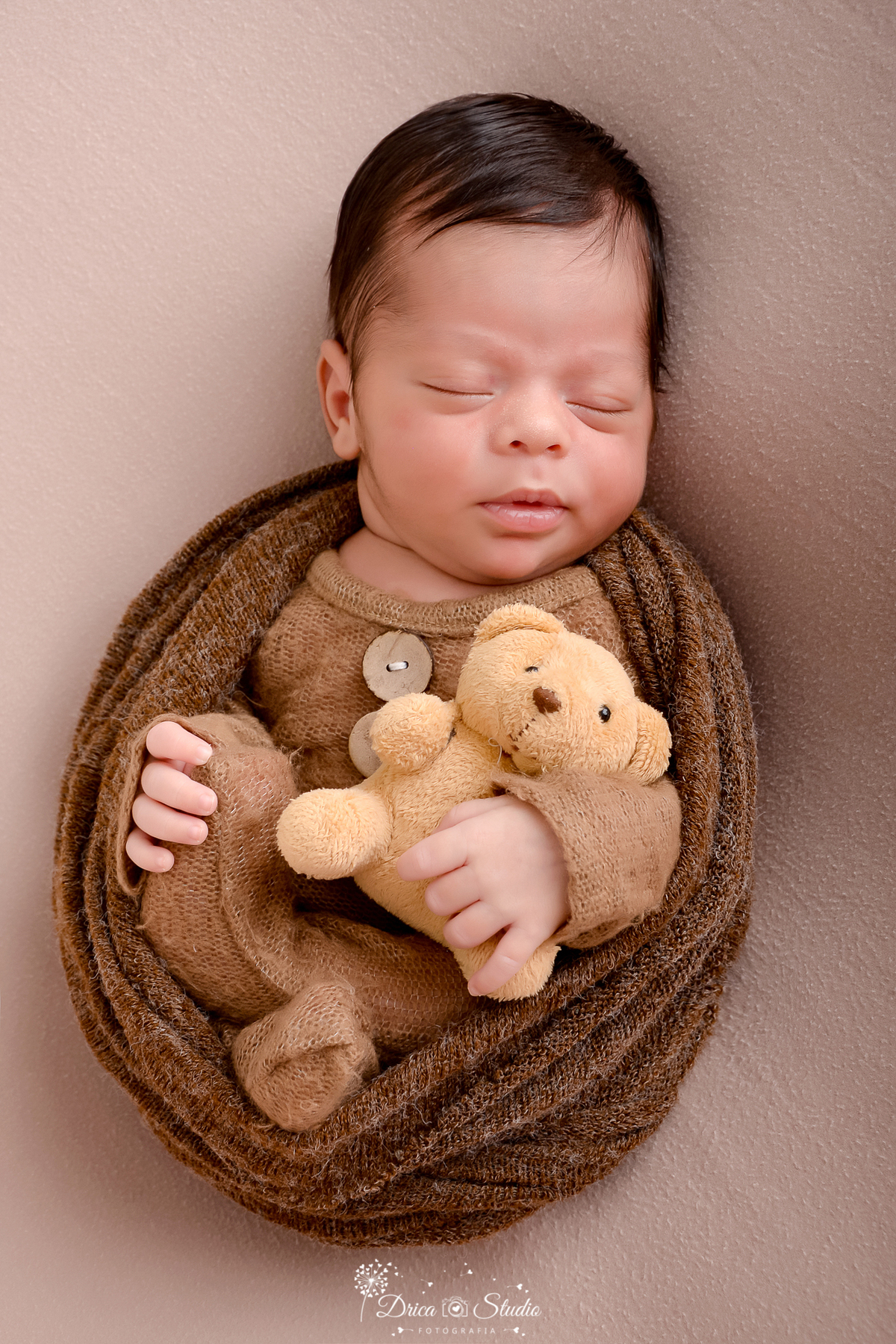 drica studio - ensaio fotográfico infantil - newborn - xinguara - bebê recém-nascido vestindo macacão marrom de tricô, envolvito em manta de tricô marrom, segurando ursinho de pelucia amarelo, deitado sobre superficie macia em cor neutra.