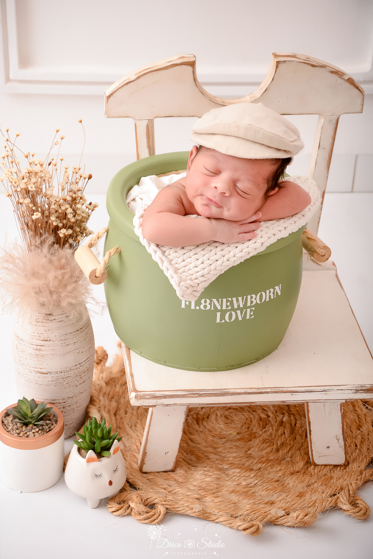 drica studio - ensaio fotográfico infantil - newborn - xinguara - bebê recém- dormindo dentro de balde verde, apoiado sobre mante de tricô creme, ele usa boina creme, decoração rústica com flores seca e cadeira de madeira branca desgastada