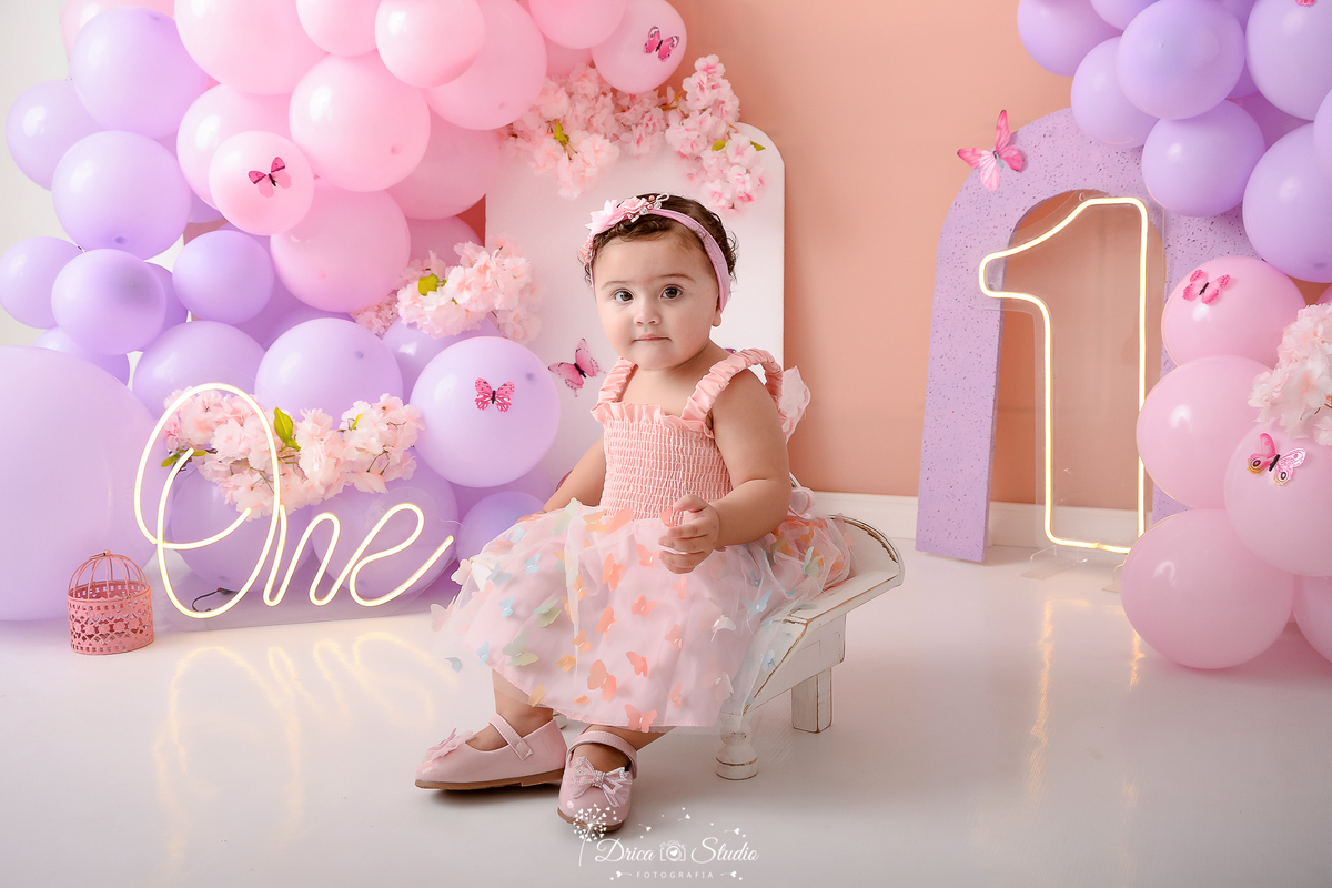 drica studio - ensaio fotografico infantil- smash the cake - jardim de borboletas - bebê sentanda em banquinho de madeira branco, usa vestindo rosa com tule e detalhes de borboletas - fundo neutro - one de led - flores de cerejeira rosa - hom de led