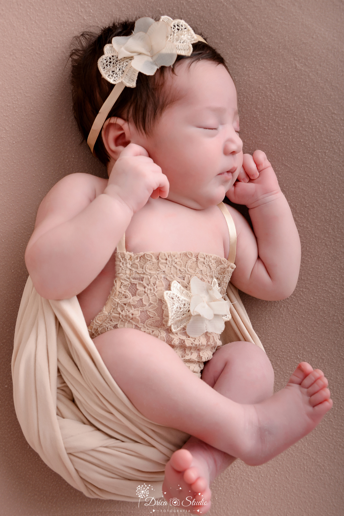 drica studio - ensaio fotografico infantil - newborn - xinguara - recém nascido envolvido em manta bege, vestindo bory com aplique na frente e tiara bege na cabeça - fundo neutro