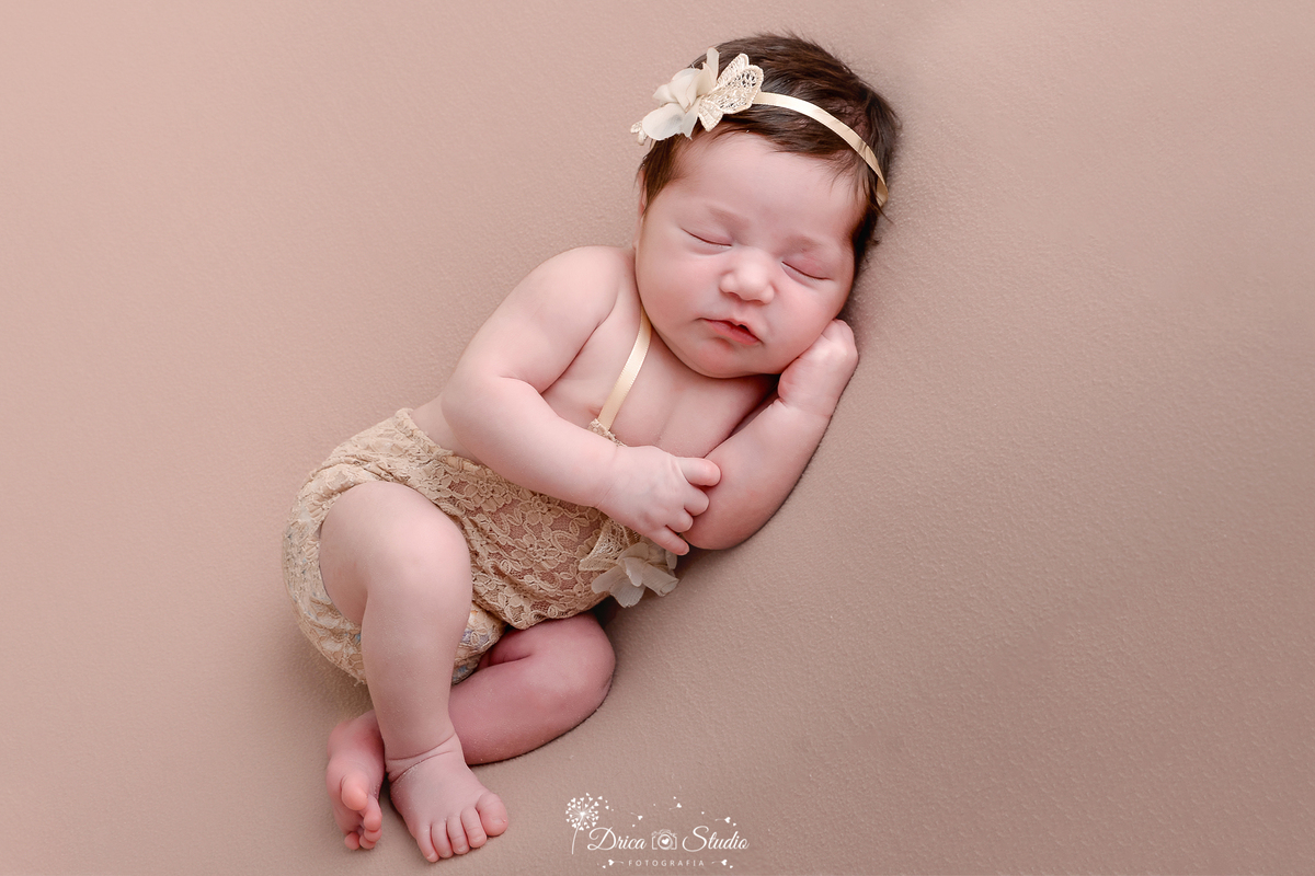 drica studio - ensaio fotografico infantil - newborn - xinguara - recém nascido deitado sobre superfice marcia, vestindo bory bege com aplique na frente, tiara com aplique na cabeça - fundo bege