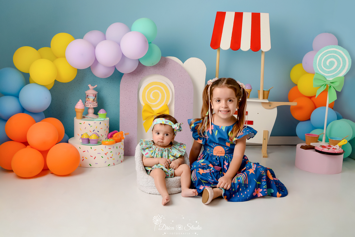 drica studio - ensaio fotográfico infantil - xinguara - acompanhamento mensal -  mundo doce - bebê sentada em poltrona e irmã mais velha sentado no chão  - balões coloridos - carrinho de sorvete branco com listra vermelho - bolo fake - arco lilás 
