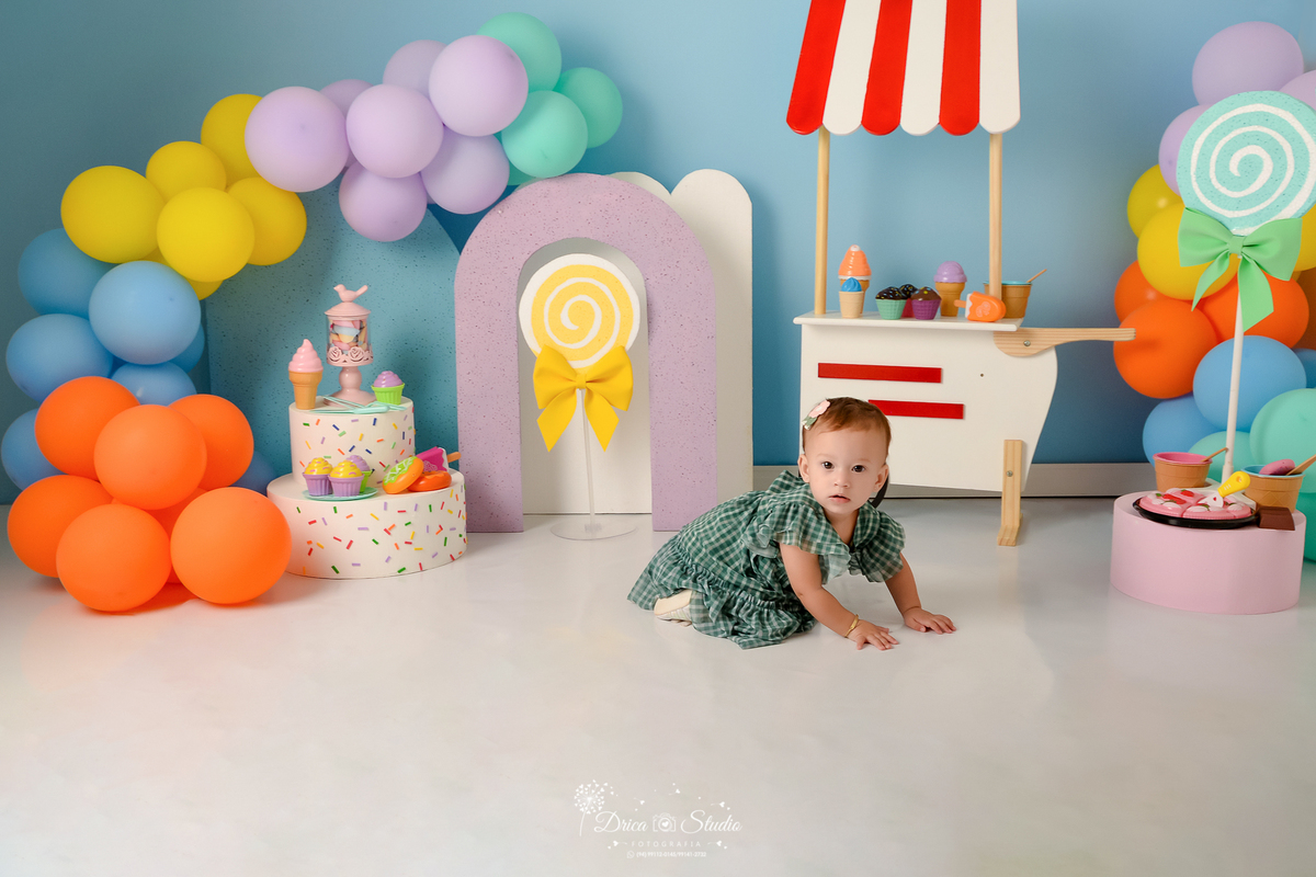 drica studio - ensaio fotográfico infantil - xinguara - acompanhamento mensal - mundo doce - bebê engatinhando - carrinho de sorvete - fundo azul claro - balões coloridos - pirulitos e bolos fake - sorvete, picoles, torta e docinho de brinquedo - 