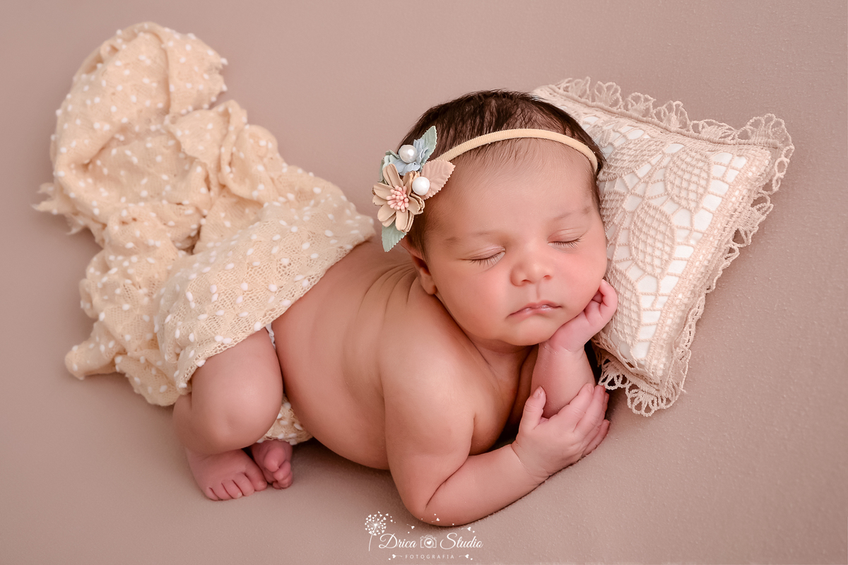 drica studio - ensaio fotográfico infantil - newborn - xinguara - bebê deitada em posição fetal, coberta com manta bege clara, apoiando o rosto sobre a mão e encostada em um travesseiro com detalhes em renda - fundo bege