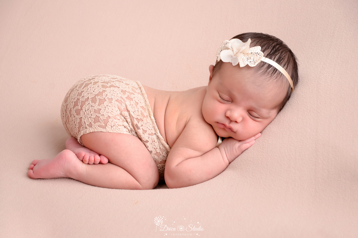 drica studio - ensaio fotográfico infantil - newborn - xinguara - bebê deitada de bruços em posição fetal, vestindo bory bege e com tiara de flores bege na cabeça - fundo bege