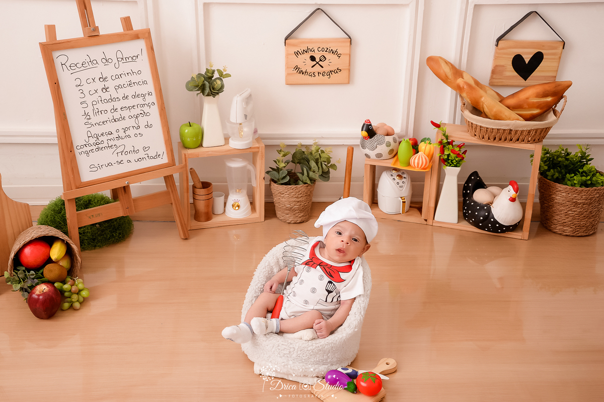 drica studio - ensaio fotográfico infantil - acompanhamento mensal - bebê sentado em poltrona branca, vestindo roupa de chef de cozinha - utensilios de cozinha - cestos com arbustos, cestos com frutas - galinha com ovos decorativos - fundo branco 