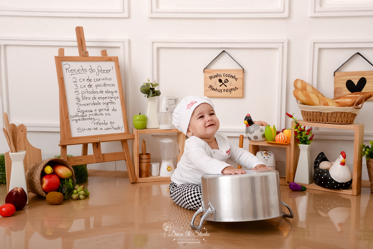 drica studio - ensaio fotográfico infantil - acompanhamento mensal- bebê sentado no chão com as mão sobre uma panela emborcada- utensilios de cozinha - galinha e ovos decorativo - fundo branco com boiserie - piso amadeiradodrica studio - ensaio fotográfic