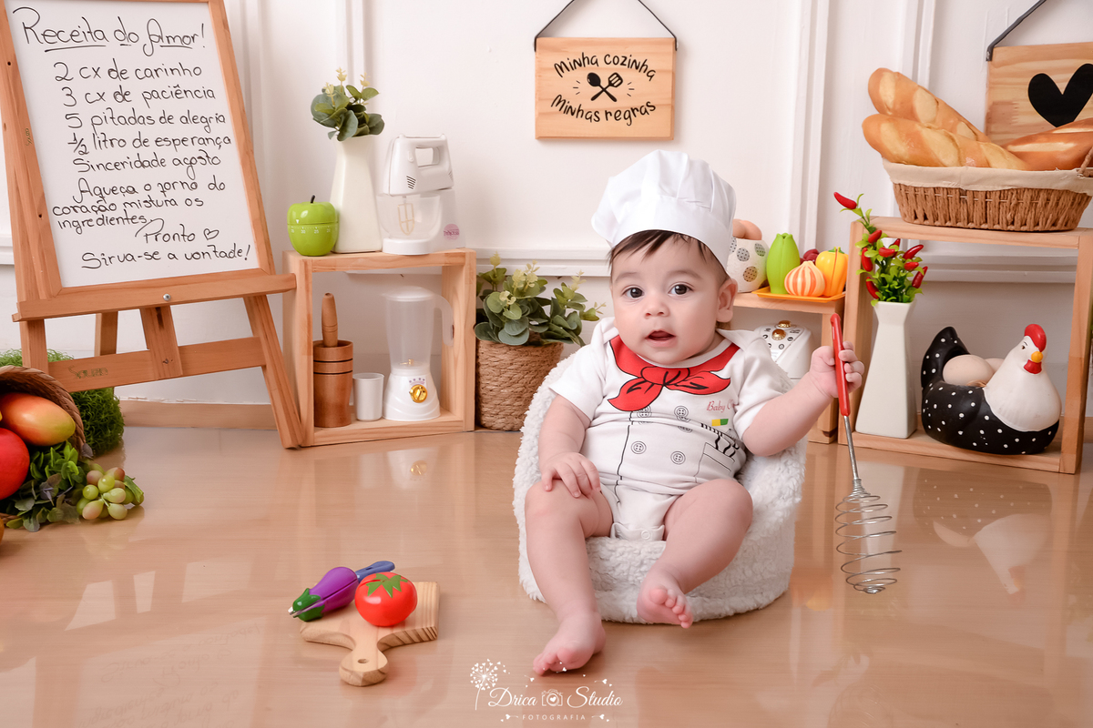 drica studio - ensaio fotográfico infantil - acompanhamento - bebê sentado em poltrona branca - cesto com frutas - pilão - liquidificador, batedeira e panela eletrica decorativa - placa com receita - cesto com pães - quadrinhos decorativos - maça verde