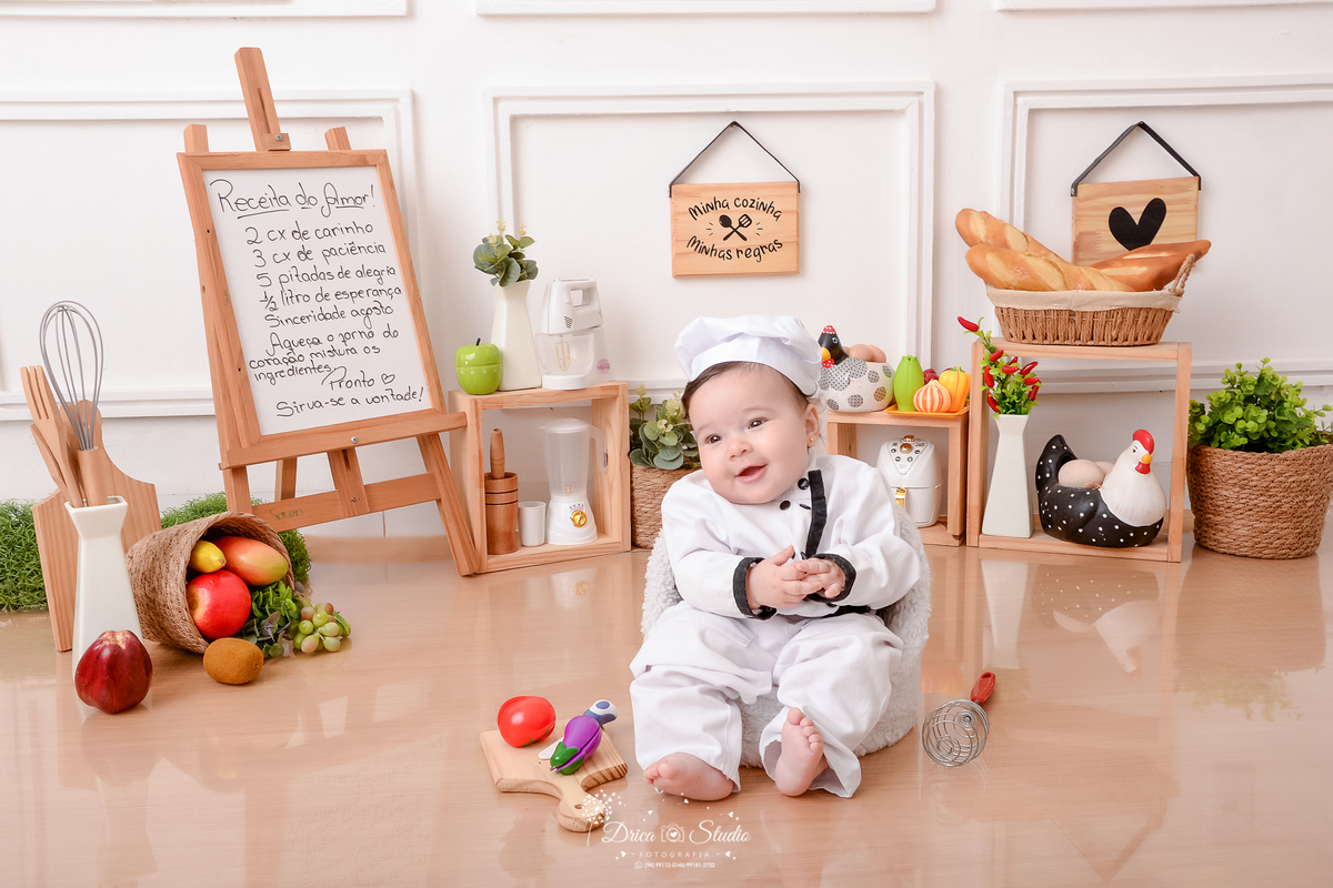 drica studio - ensaio fotográfico infantil - acompanhamento -mensal- bebê vestindo roupa de cheg de cozinha - placa com receita - utensilios de cozinha - cestos com folhagem - galinha decorativa - eletrodomertico de brinquedo - fundo branco com boiserie