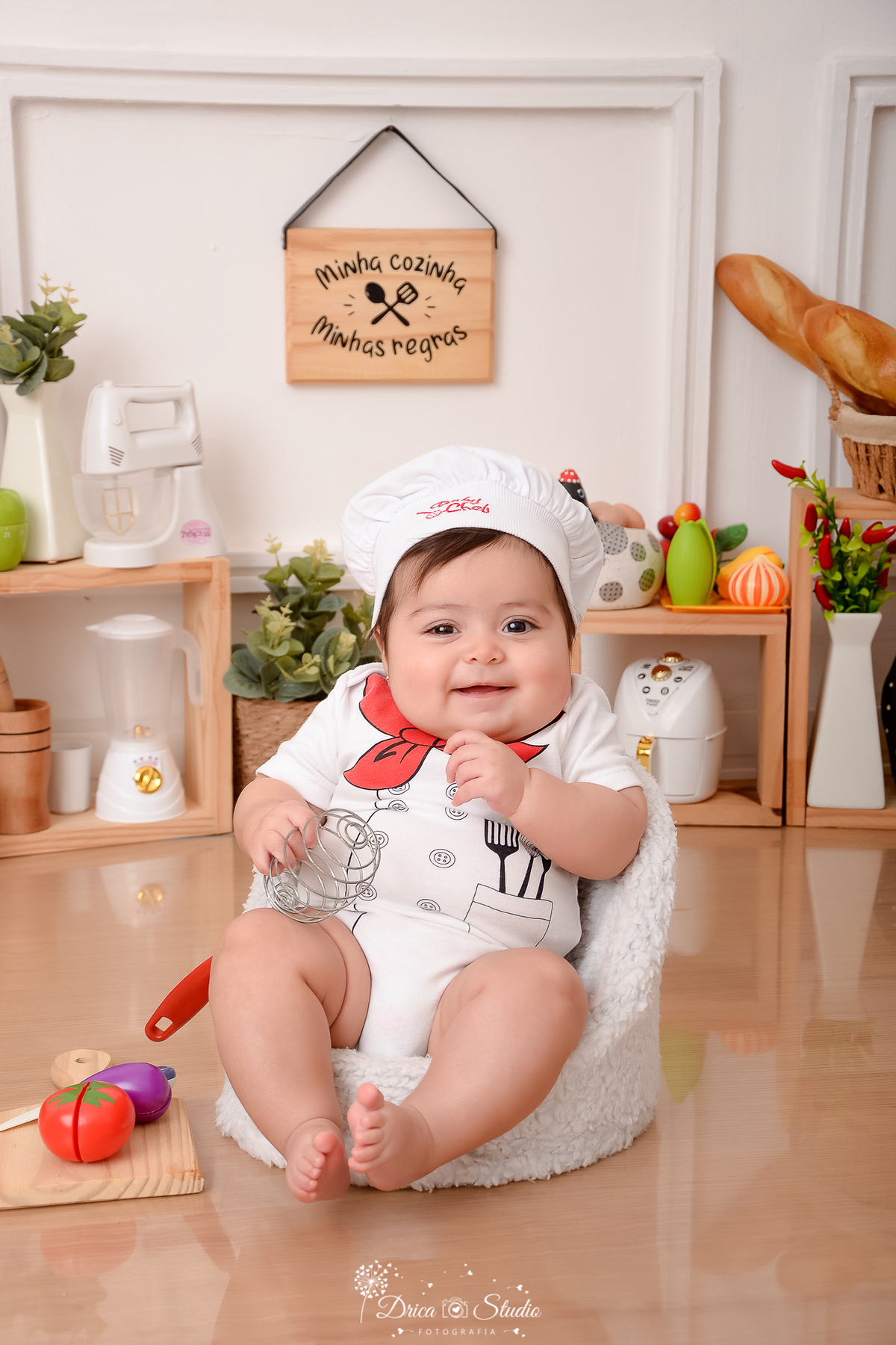 drica studio - ensaio fotográfico infantil - acompanhamento - bebê sentada em poltrona branca, vestida de chef de cozinha - liquidificador, panela eletrica e batedeiras de brinquedo - pilão - vaso branco com pimenteira - legumes e galinhas decorativas