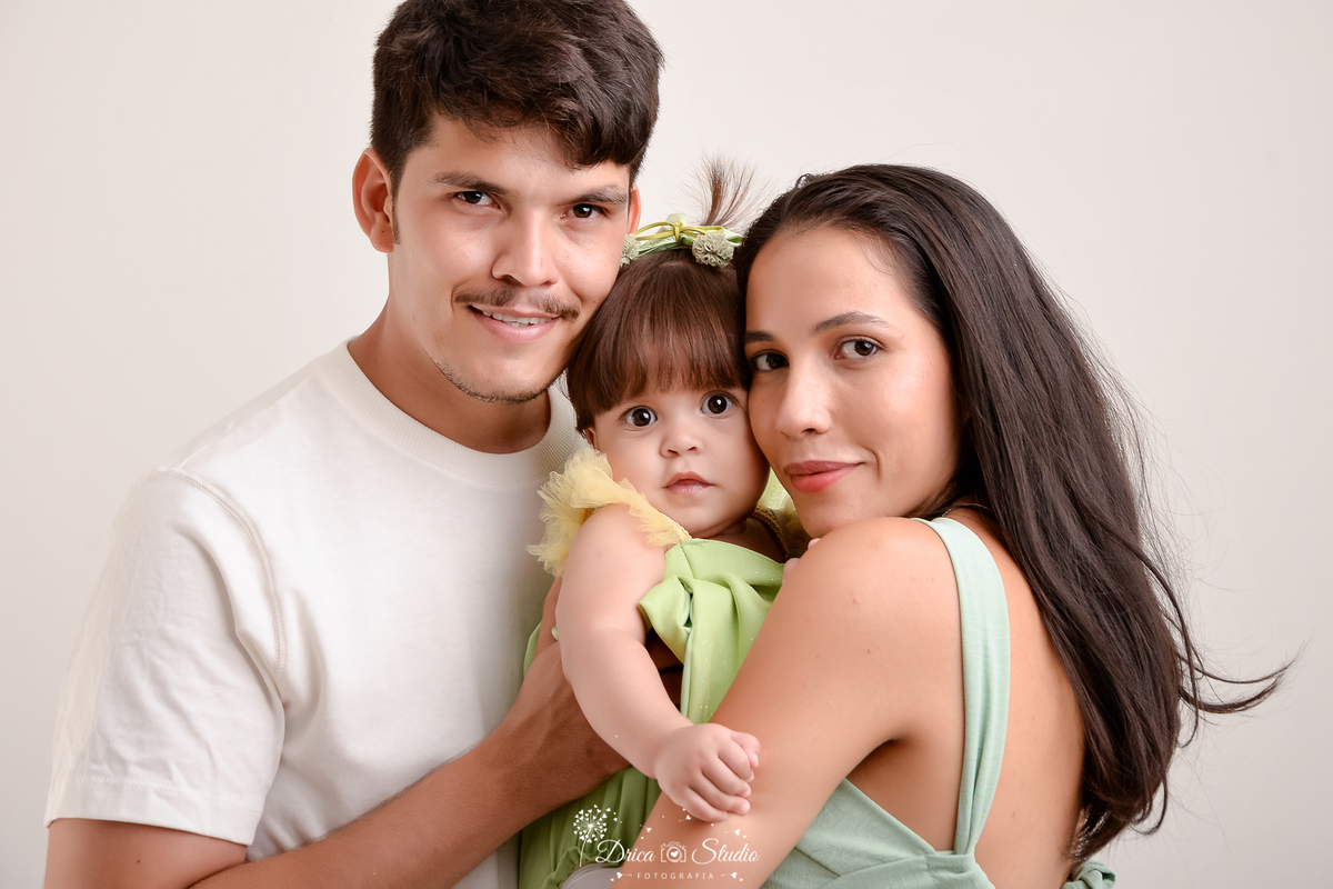 drica studio - ensaio fotografico infantil - smash the cake tinker bell - xinguara - foto em familia - casa segurando bebê fantasiada de tinker bell no colo - fundo branco - camisa branca - vestindo berde oliva