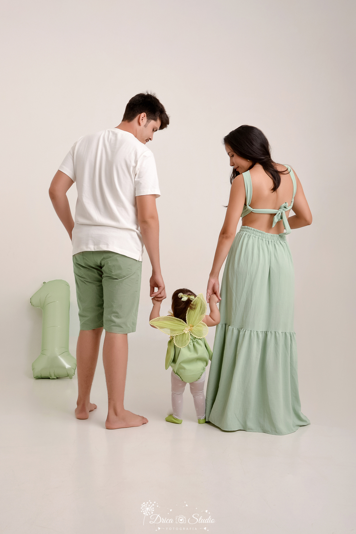 drica studio - ensaio fotografico infantil - smash the cake tinker bell - xinguara - casal de costa segurando bebê pelas mãos - hum de balão verde oliva - vestindo verde oliva - camisa branca e short verde oliva - fundo branco