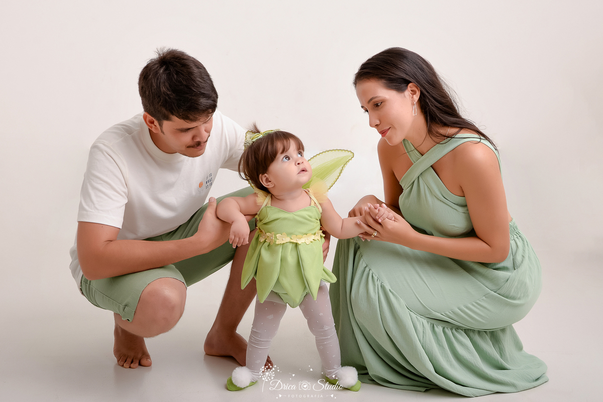 drica studio - ensaio fotografico - smash the cake - foto em família - casal segurando bebê em pé - bebê vestindo fantasia da tinker bell - vestindo longo verde oliva - camisa branca e short verde oliva - xinguara - fundo branco