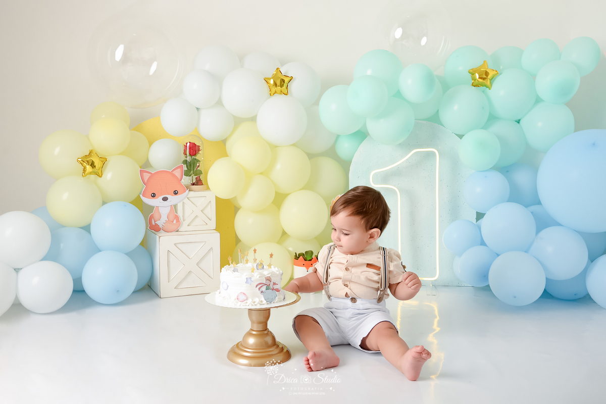 drica studio - ensaio fotográfico infantil - smahs the cake pequen principe - xinguara - bebê sentado no chão, vestindo camisa bege clara e short branco com suspensário degustando bolo com glacer branco - rosa dentro de uma cúpula de vidro -caixas branca