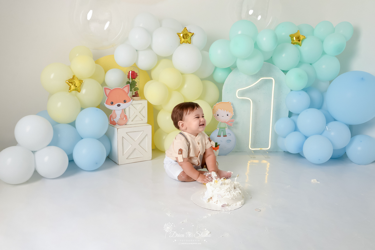 drica studio - ensaio fotográfico infantil - smahs the cake pequen principe - xinguara - Bebê sorridente sentado no chão - bolo branco - balões azul, amarelo, verde agua e branco - hum de led - painel azul claro - fundo branco