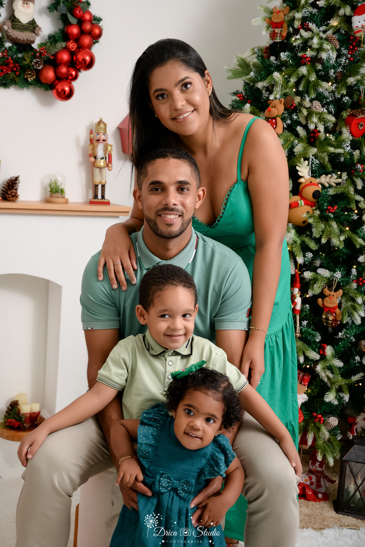 drica studio - ensaio fotografico - xinguara - fotos de natal - vestidos verdes - camisa gola polo verde e calças caqui - casal com filhos pousando para fotos - árvore de natal - lareira branca - quebra nozes - fundo branco
