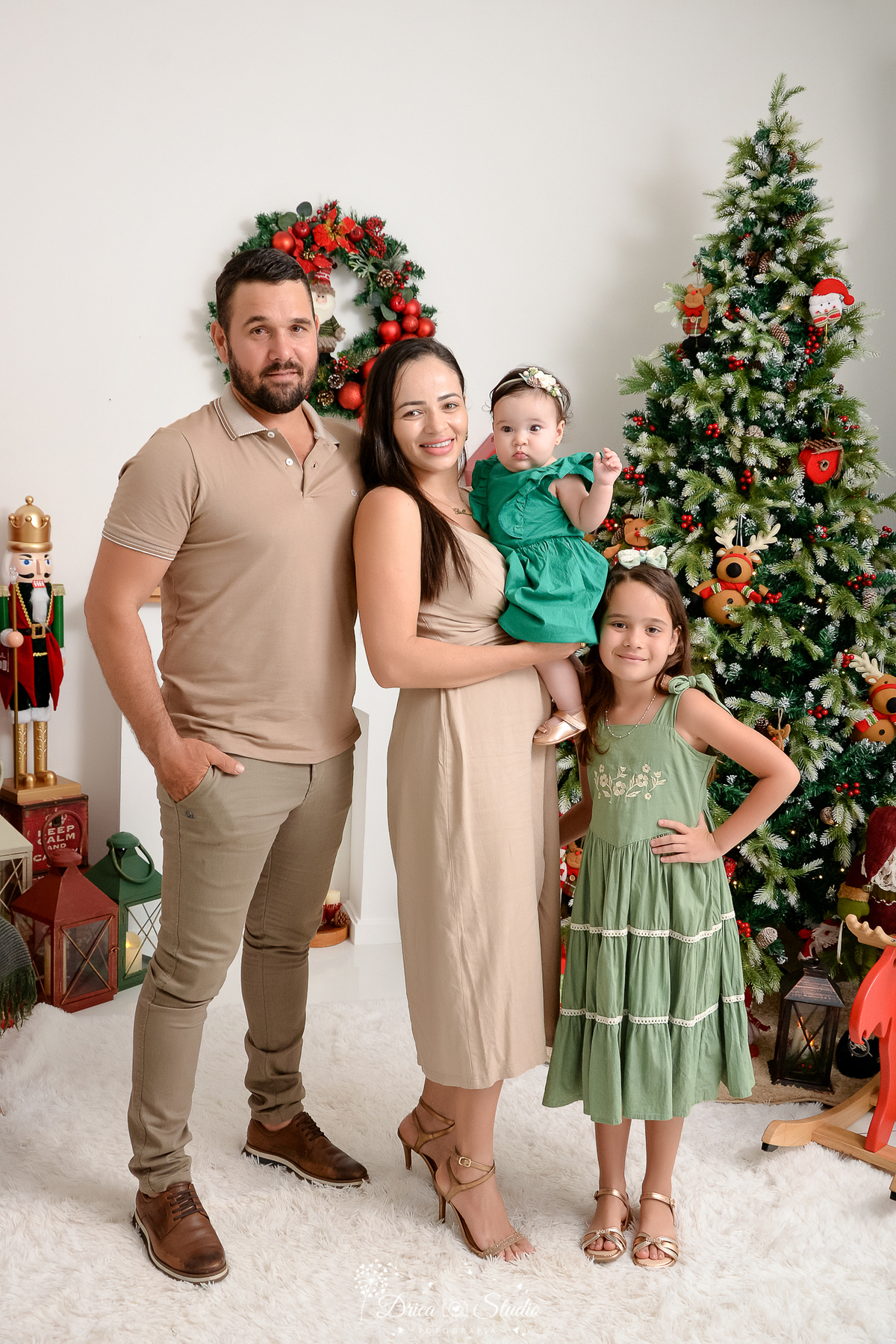 drica studio - ensaio fotográfico - xinguara - pará fotos de natal - casal pousa para fotos com as duas filha, bebê veste vestido verde menta e irmã vestido verde oliva, pai camiseta e calça bege e mãe vestido bege - decoração de natal - árvore de natal