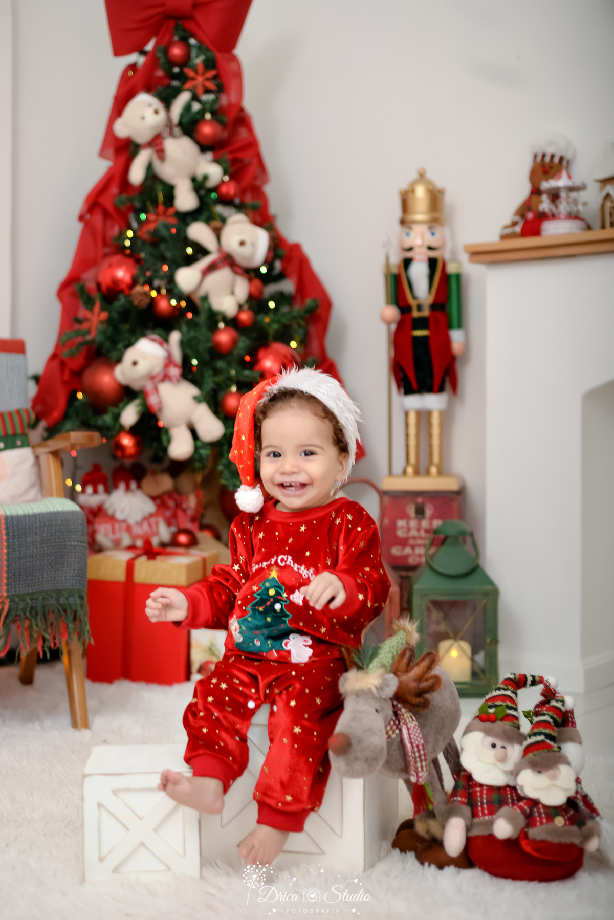 drica studio - ensaio fotografico - xinguara - fotos de natal - bebê vestindo macaquinho vermelho e gorro vermelho de natal, sentando em cima de caixotes de madeira branco - quebra nozes - lampiões - presentes - ursinho de natal - fundo branco