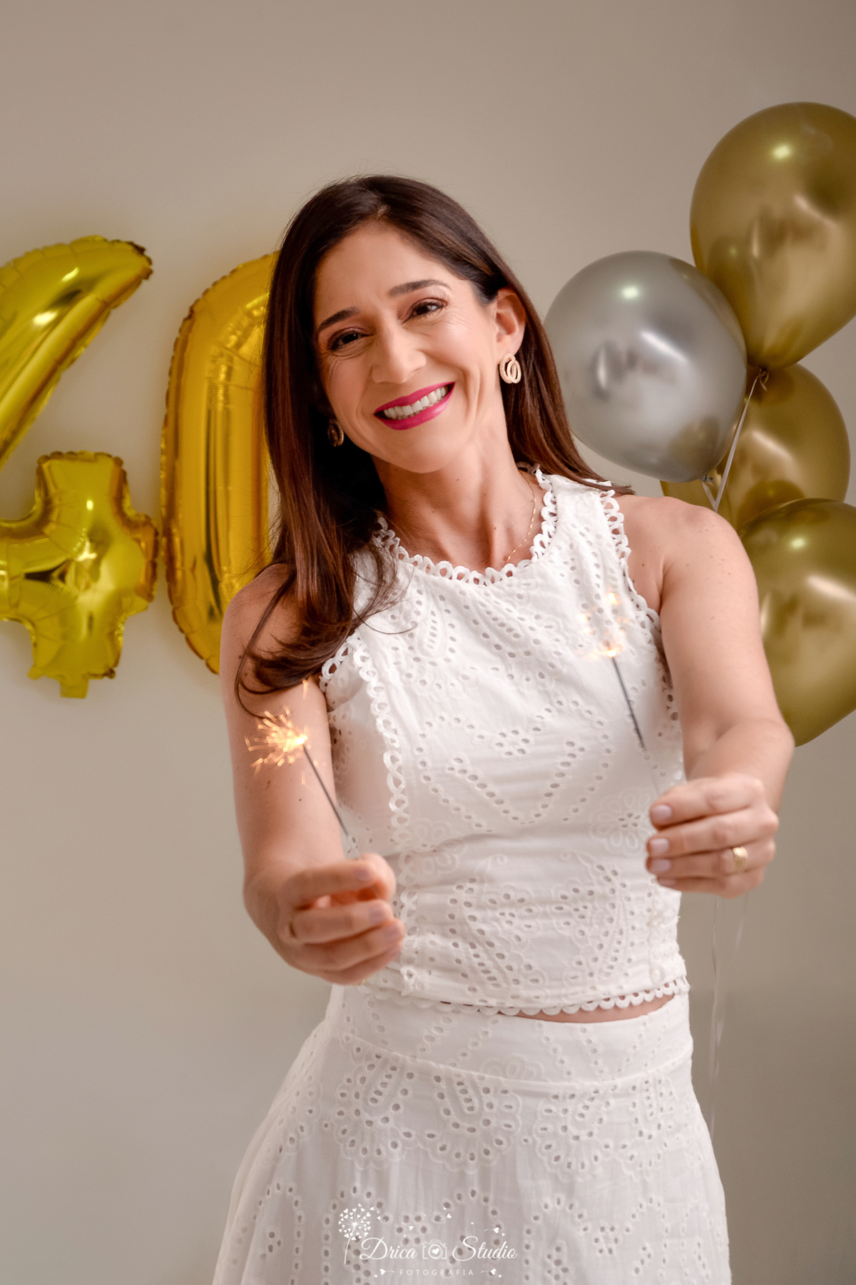 drica studio fotográfico - ensaio aniversário 40 anos - xinguara - pará - mulher usando vestido longo branco, segurando velinhas de faisca - número 40 de balão dourado - balões dourados e prateado - fundo neutro