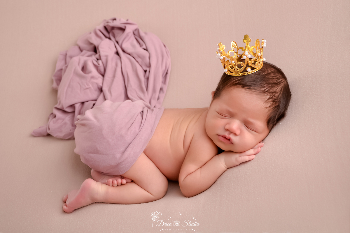 drica studio fotográfico - ensaio newborn - xinguara - pará - bebê recém-nascida deitada de bruço usando uma coroa dourada na cabeça, com manta sobre suas costa - fundo neutro