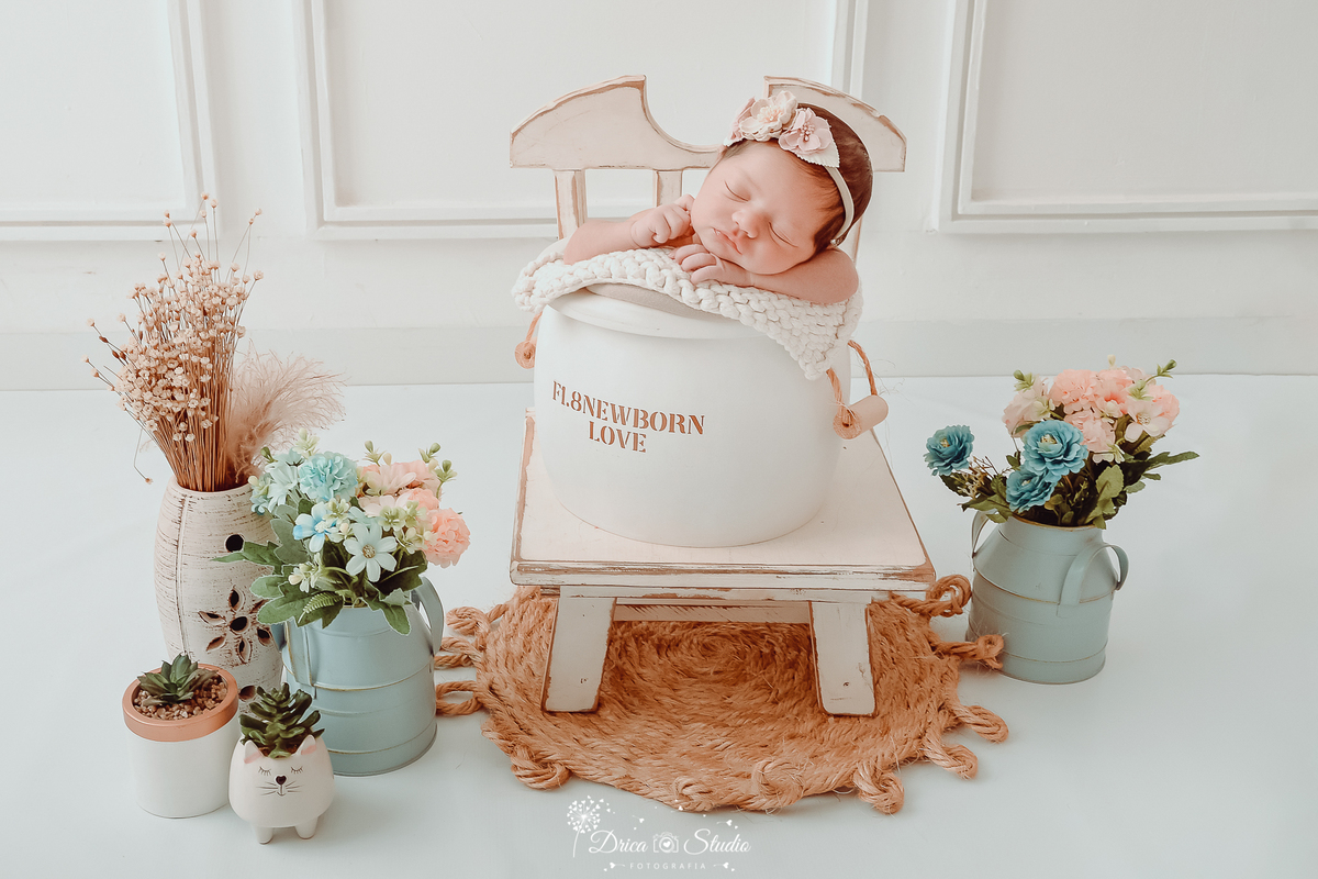 drica studio fotográfico - ensaio newborn - xinguara - pará - bebê recèm-nascido dentro de baldinho branco de madeira - usando faixinha de flor na cabeça - vasos azuis com flores azul e rosa, vasos branco com flores secas - fundo branco com boiserie