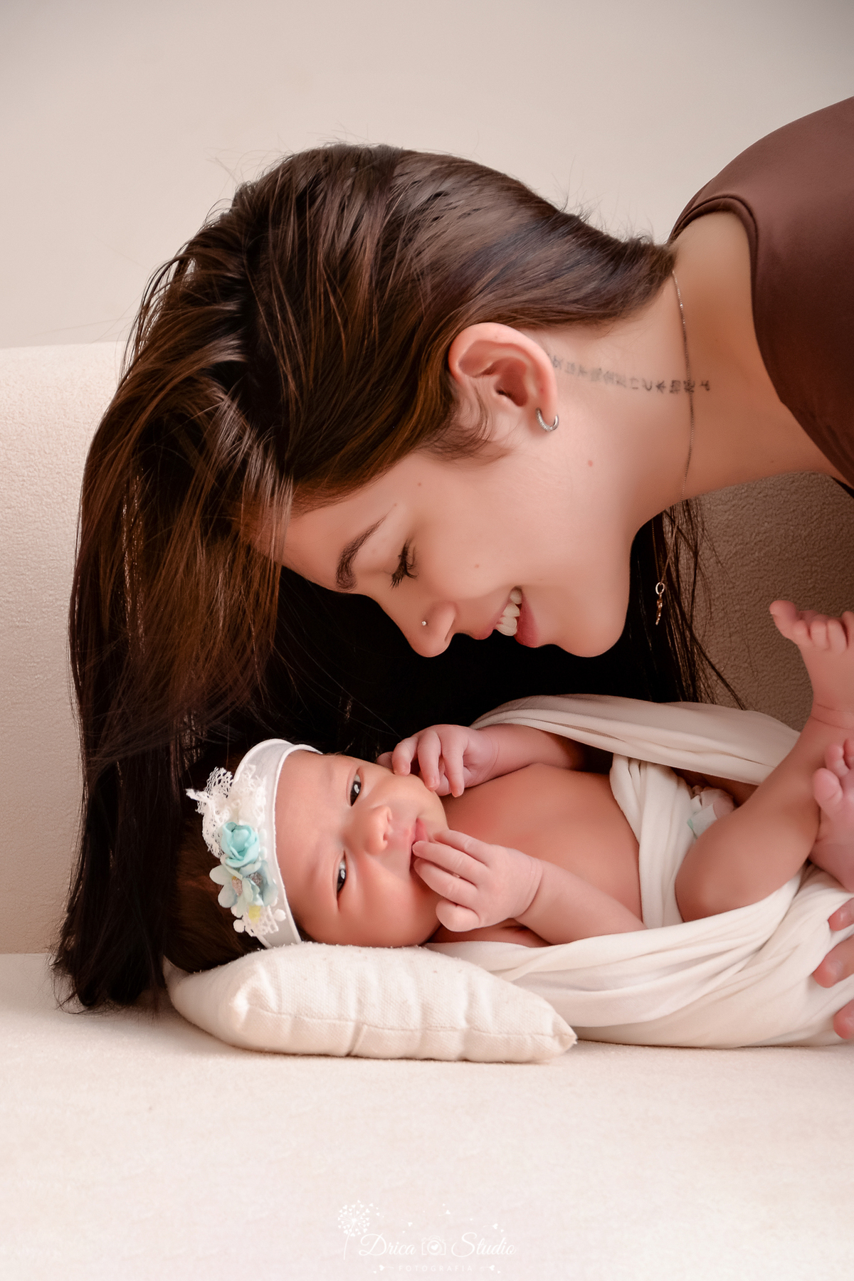 drica studio fotográfico - ensaio newborn - xinguara - pará -bebê recèm-nascida deirtada sobre estofado envolvida da manta clara, com pézinho cruzado e mão na boca, sobre ela mãe que a olha com carinho - fundo neutro