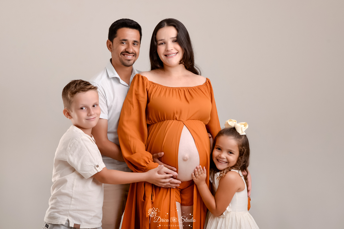 drica studio - ensaio fotográfico gestante - xinguara - pará - familia em ensaio de gestante em estúdio, vestido longo terracota com cauda, ambos acareciam a barriga da gestante - fundo neutro