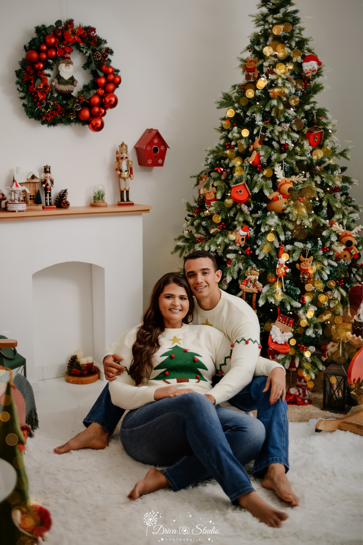 drica studio -ensaio fotografico-Casal posando em cenário natalino completo com árvore de Natal e decoração temática, ensaio fotográfico em estúdio profissional.