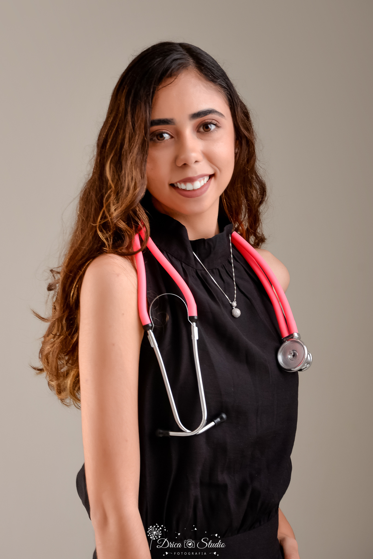 drica studio - ensaio fotografico - formatura - xinguara - pará- jovem usando blusa preta e sobre seus ombro um estetoscópio rosa - fundo neutro