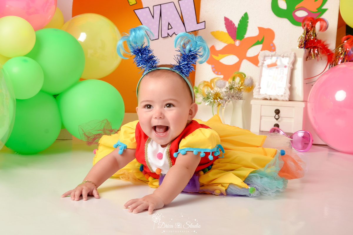 drica studio - ensaio fotográfico infantil - carnaval- xinguara - pará - bebê usando vestido de palhacinha - tiara com coqueiros azuis - máscara de carnaval - balões coloridos - fundo amarelo - nome CAR NA VAL