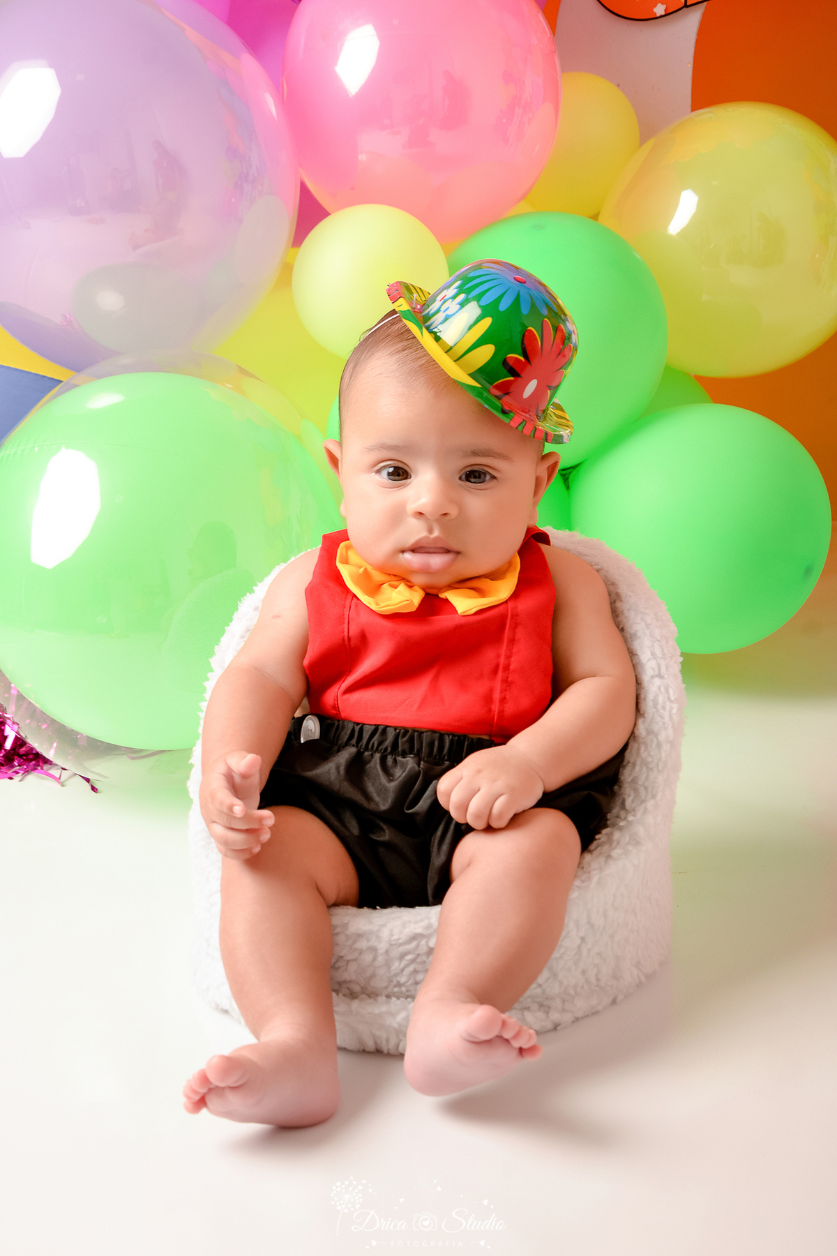 drica studio - ensaio fotográfico infantil - carnaval- xinguara - pará - bebê sentado em poltrona vestido de palhaçinho e chapéu colorido - balões verde e amarelo - fundo amarelo