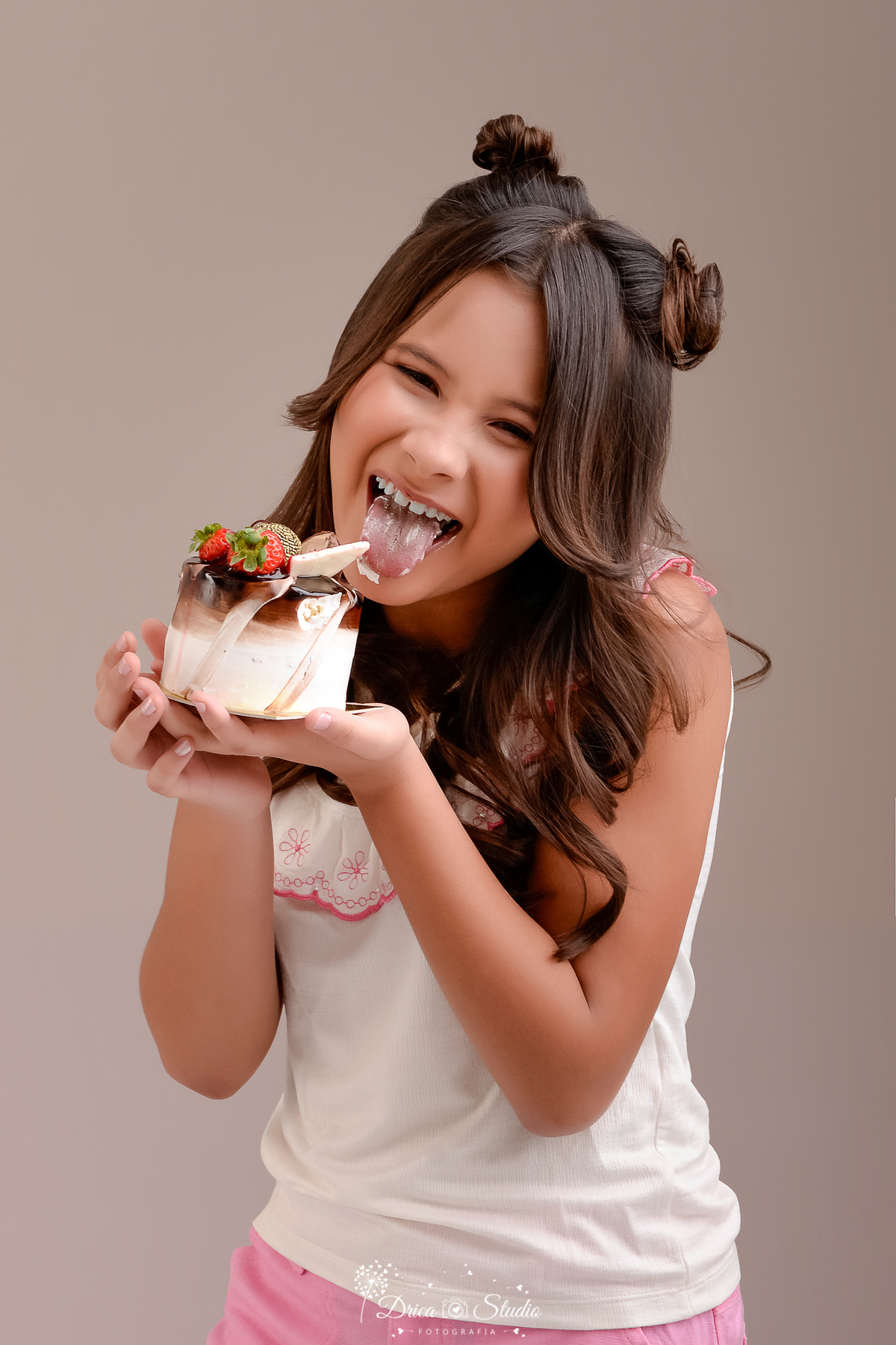 Drica studio - ensaio fotografico infantil - xinguara - pará - Foto divertida de aniversário 11 anos, menina lambendo cobertura de bolo decorado com morangos e chocolate, ensaio em estúdio fundo neutro.