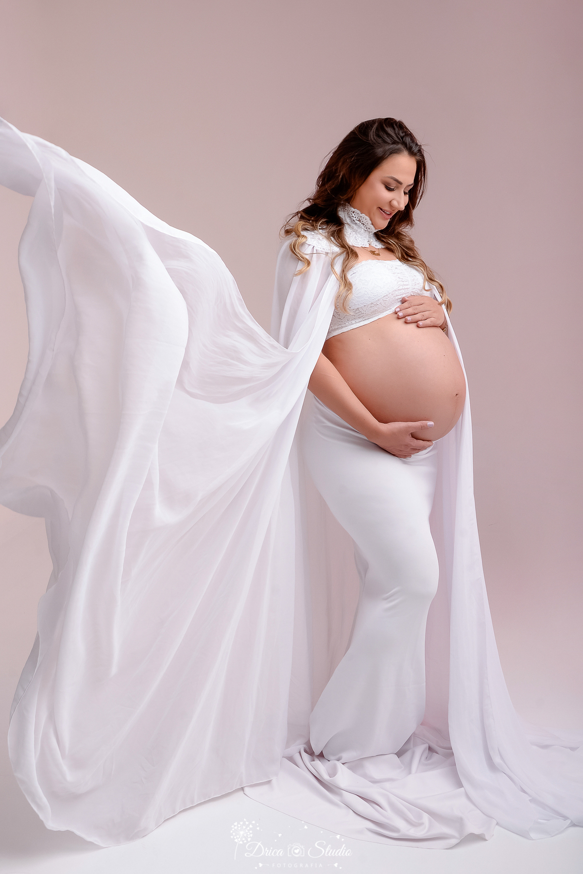 drica studio - ensaio fotografico gestação - xinguara - pará - gestante usando roupa branca, com envolvendo a barriga com o braço - fundo neutro