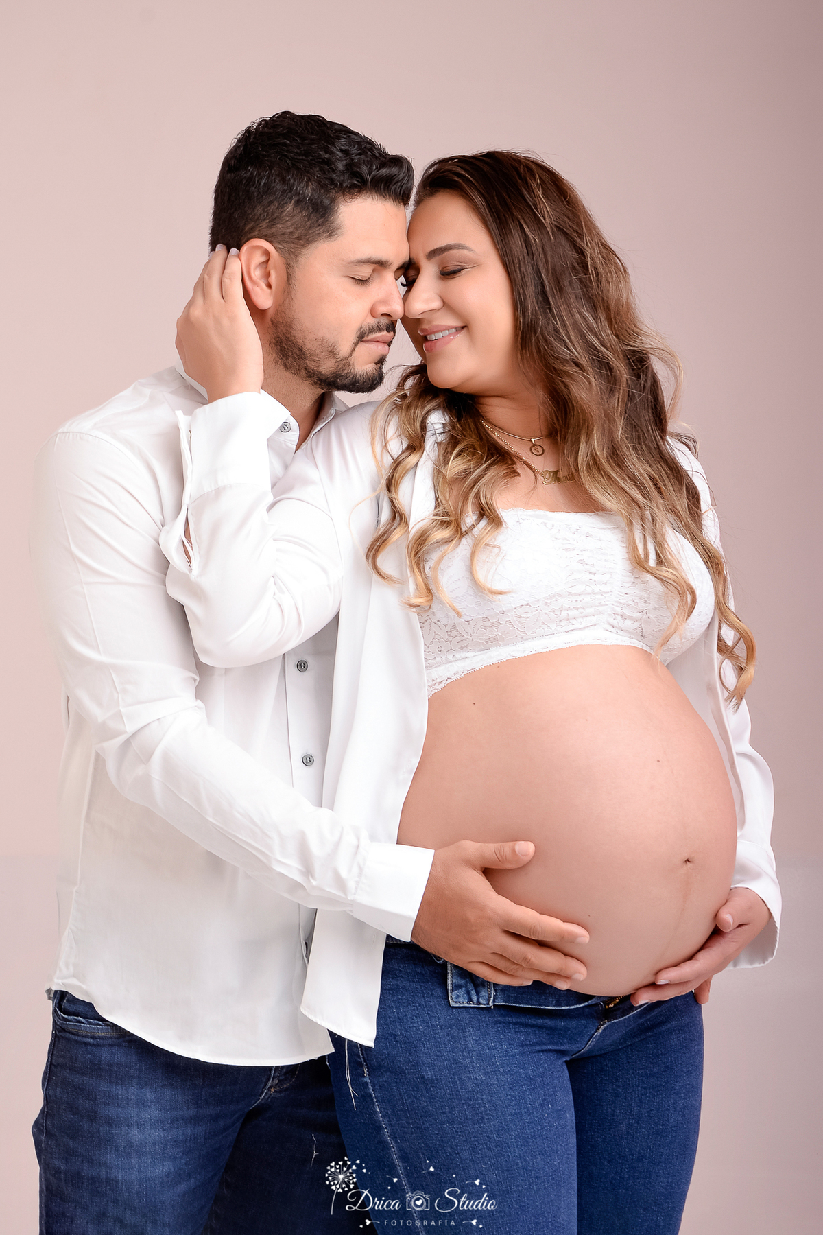drica studio - ensaio fotografico gestação - xinguara - pará - casal posam para fotos gestacional - usam roupas brancas, barriga gestaional a amostra - mulher encostada no ombro do esposo - fundo neutro